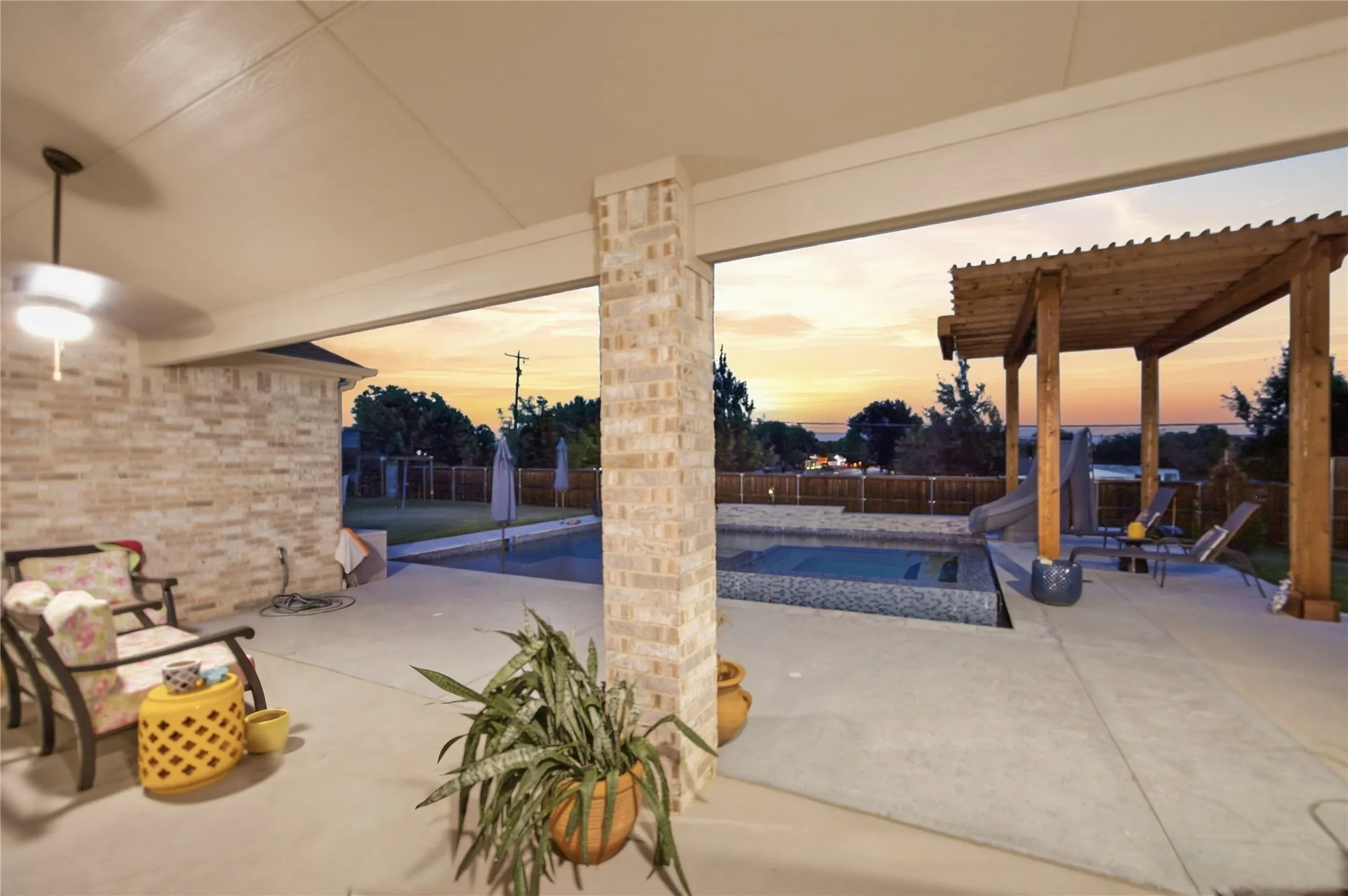 Covered patio with a ceiling fan, brick exterior wall, concrete flooring, and a swimming pool with an adjacent wooden pergola