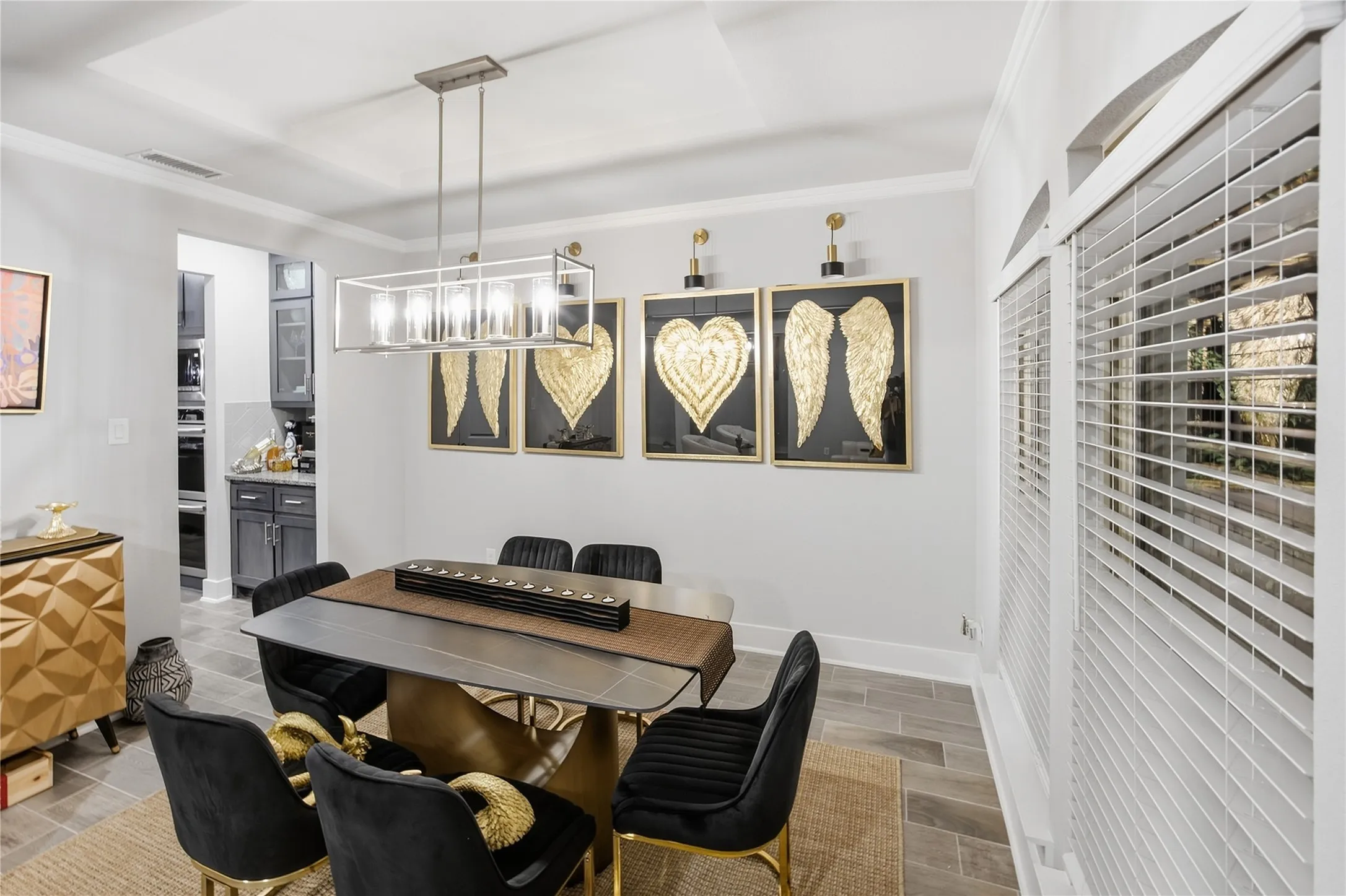 Tray ceiling with crown molding, rectangular chandelier, window with plantation shutters, wood-finish flooring, and built-in cabinetry in background