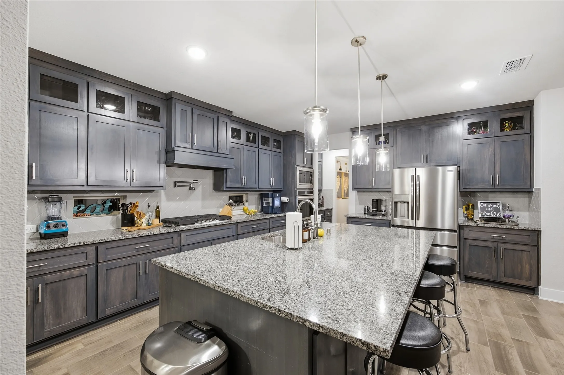 Kitchen featuring a large island with stone countertop, stainless steel appliances, extensive cabinetry with glass accents, a built-in cooktop, and wood-finish flooring