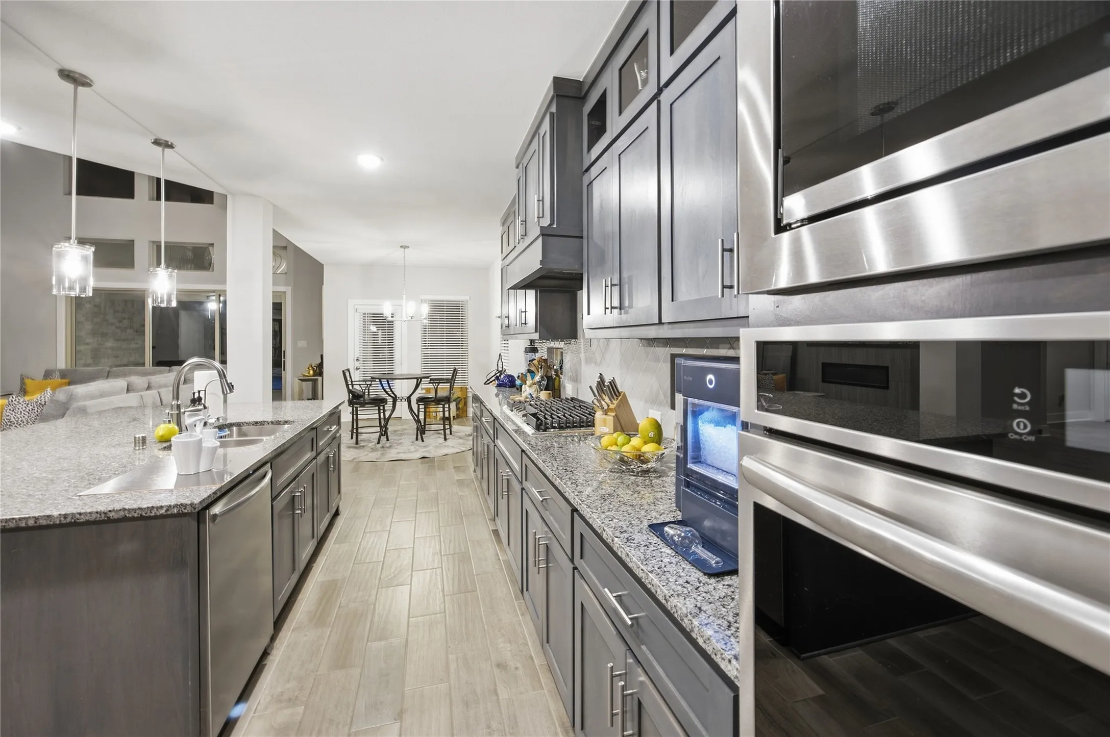 Kitchen featuring wood-finish flooring, granite countertops, stainless steel appliances, pendant lighting, and gray cabinetry