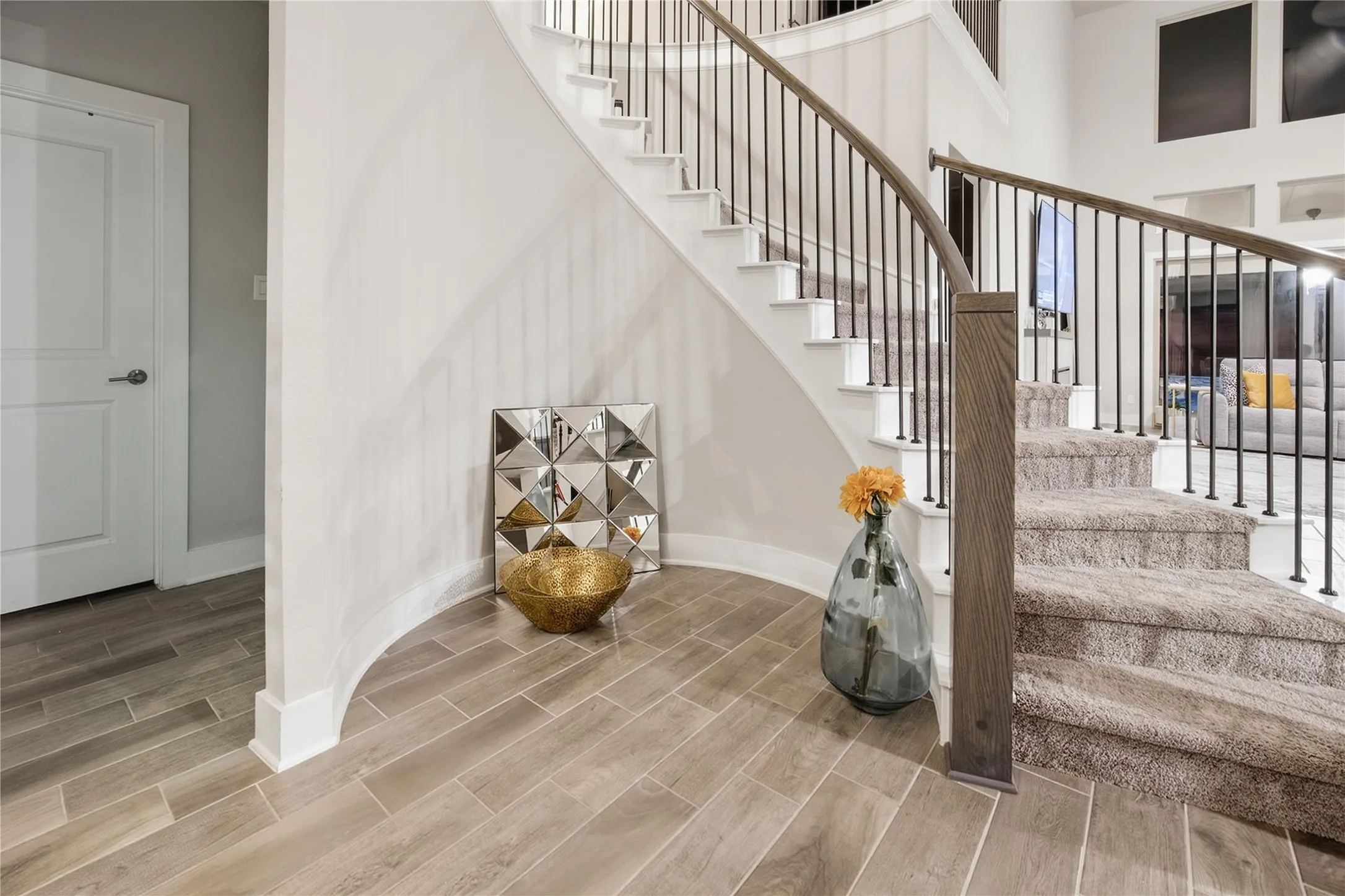 Curved staircase with wood-finish handrails and wrought iron balusters, carpeted treads, and wood-finish flooring