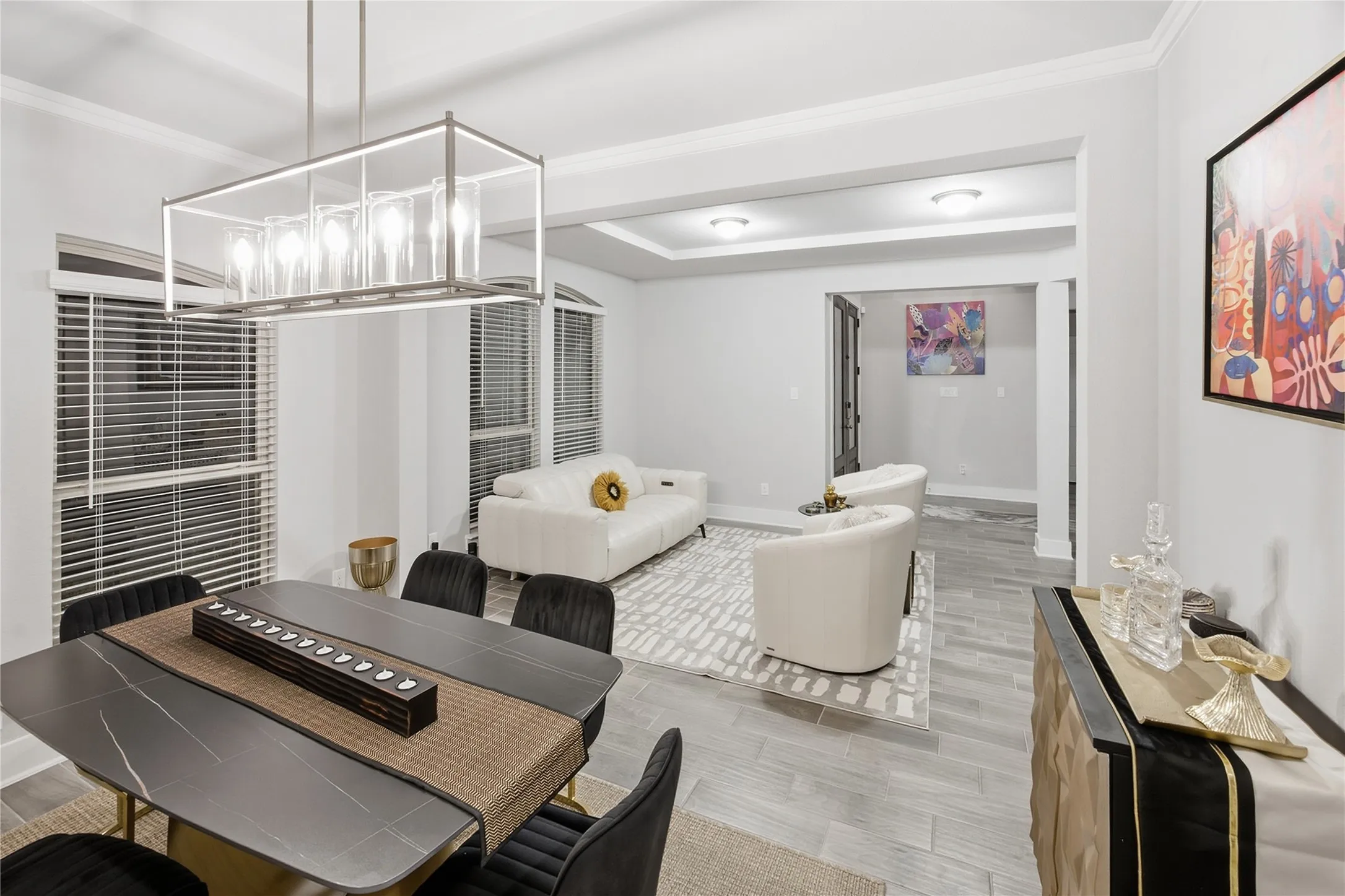 Open-concept living space with light gray walls, crown molding, a modern linear chandelier, and wood-finish tile flooring