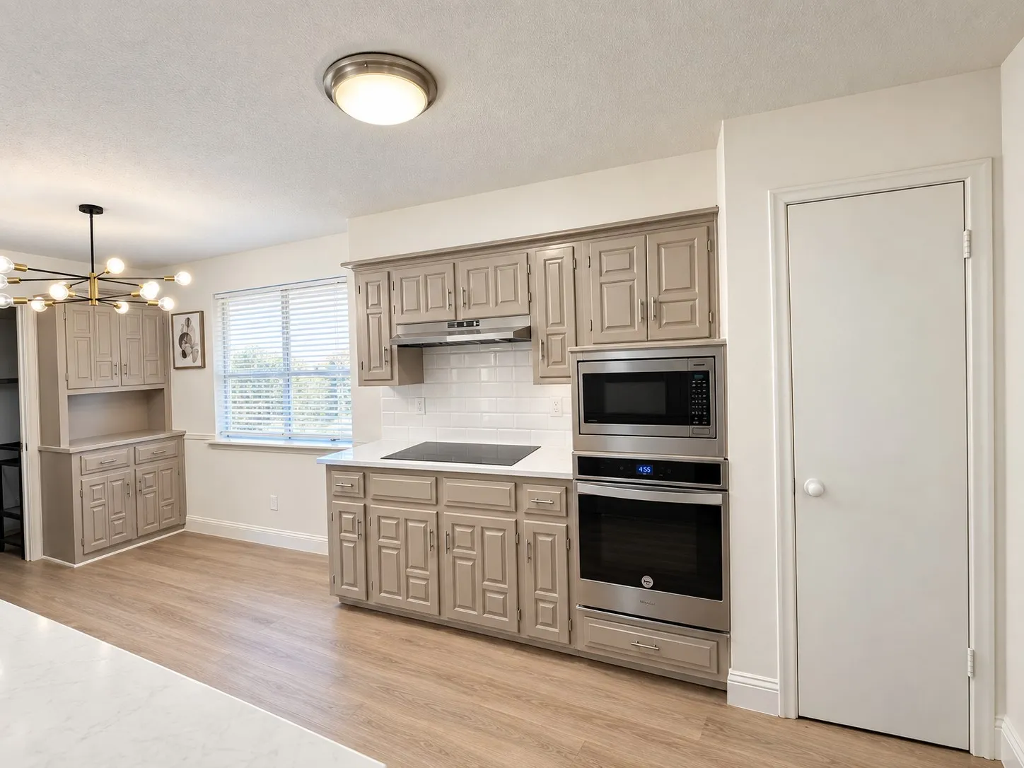 Built-in stainless steel double oven and microwave, white subway tile backsplash, white countertops, wood-finish flooring, and a built-in buffet with cabinetry