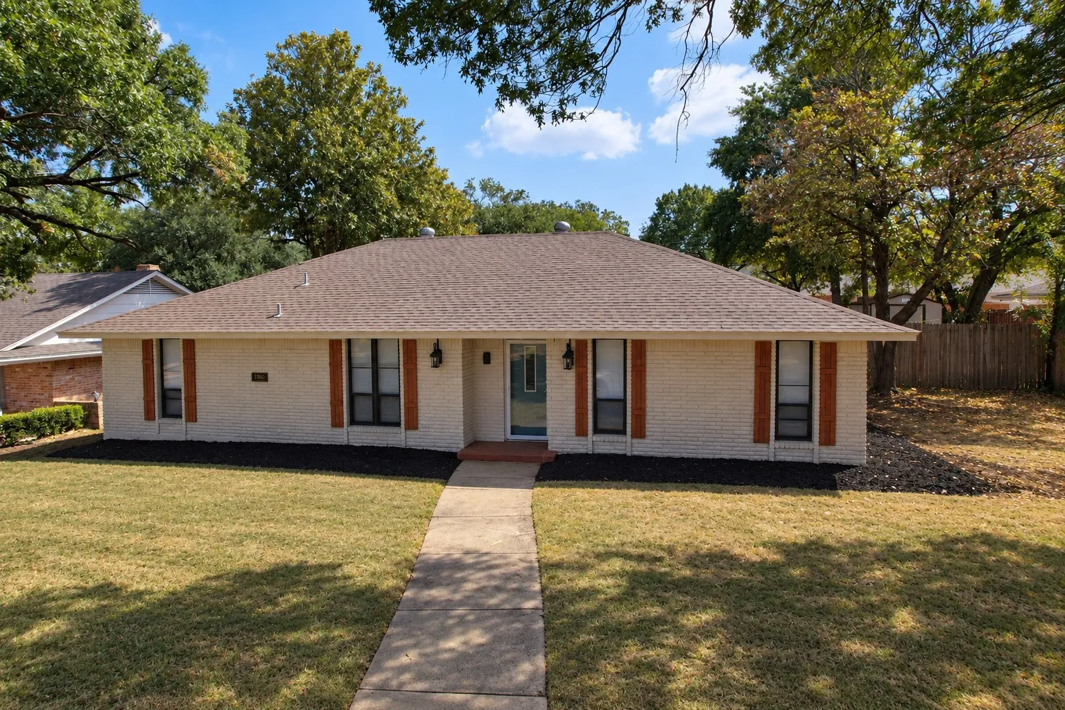 White brick exterior with a brown shingle roof, complemented by wood-finish window shutters