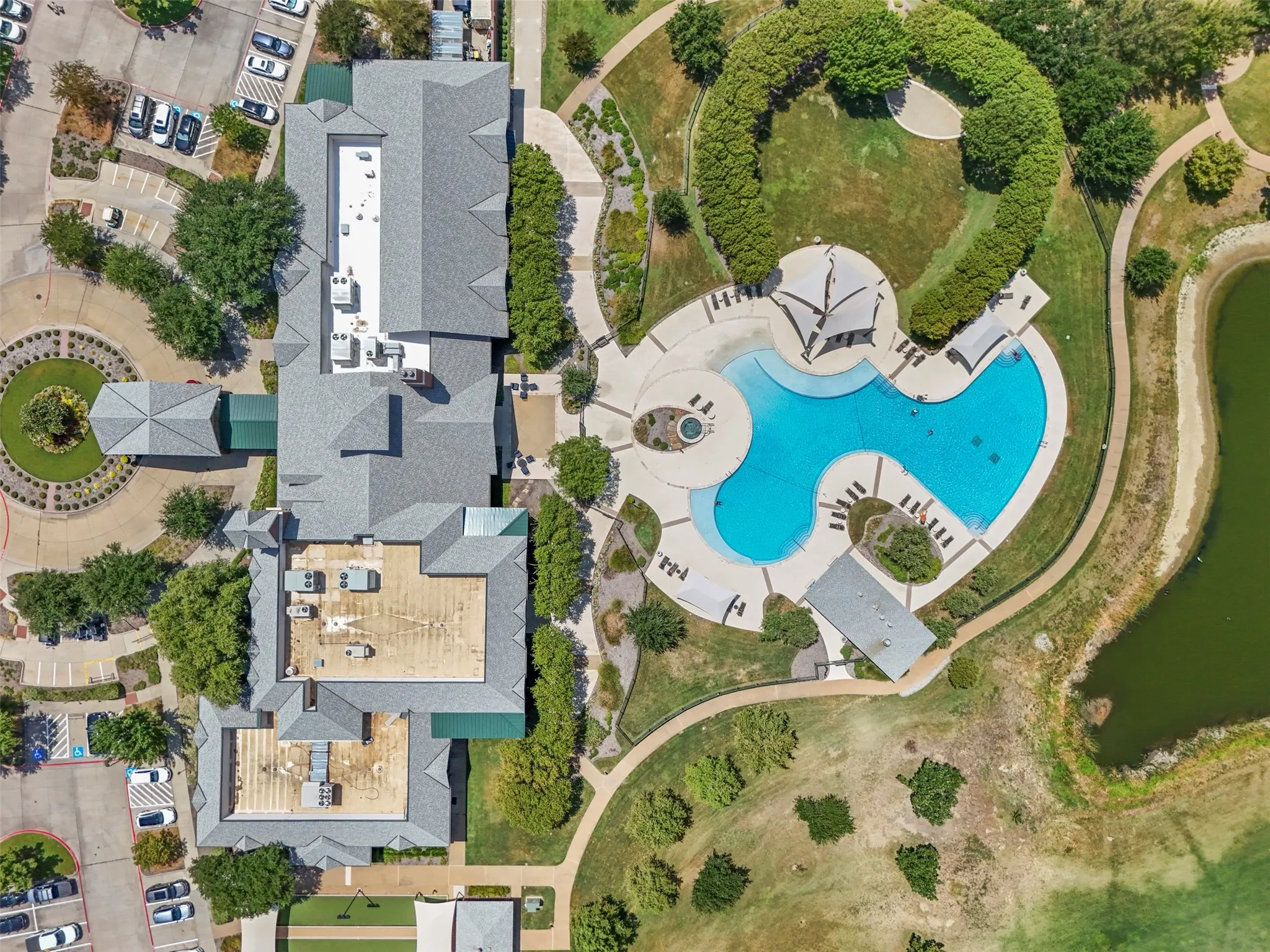 Community recreation center featuring a swimming pool, expansive paved pool deck, and shaded seating areas