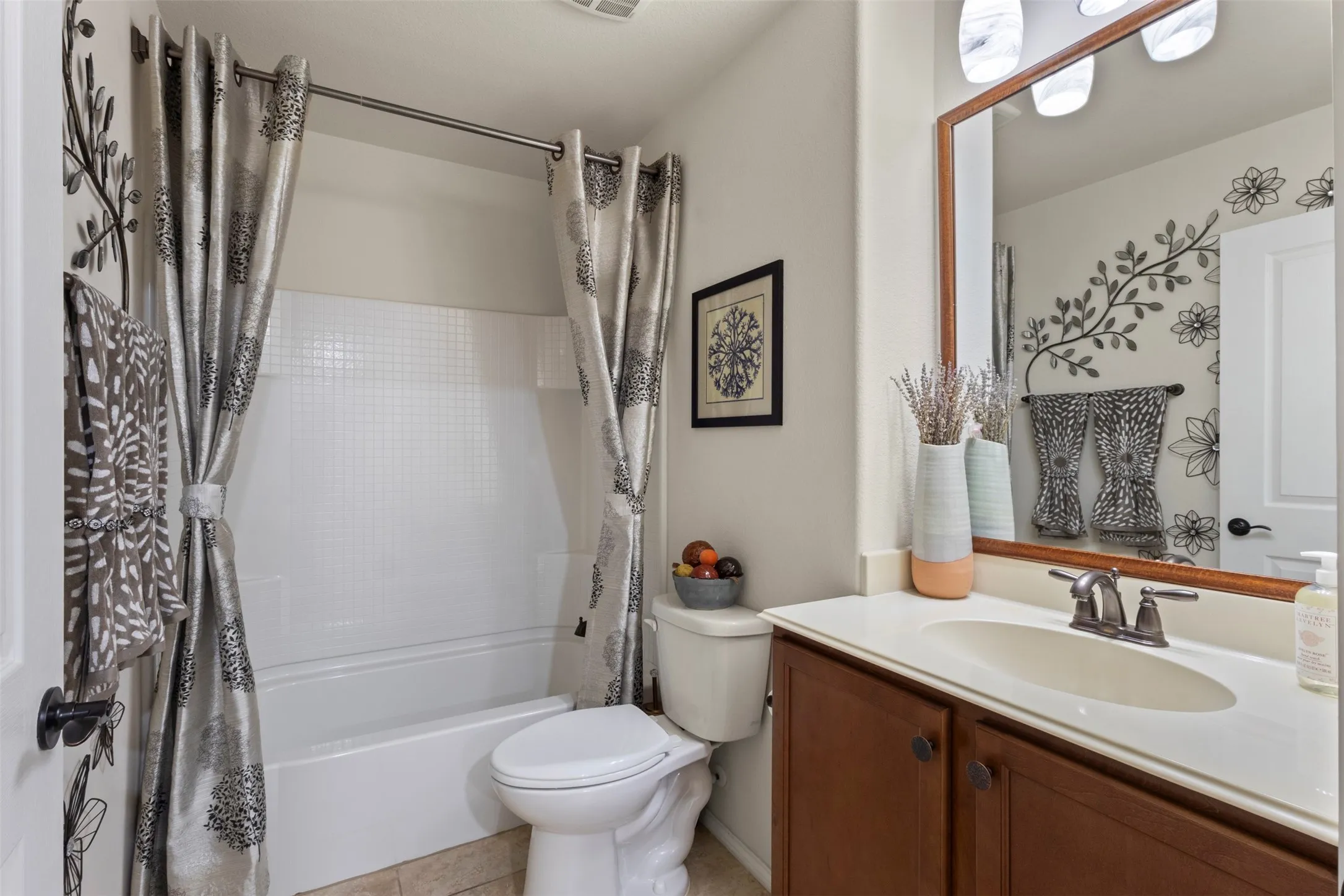Bathroom featuring a full tub with shower, single vanity with integrated sink, wood-finish cabinetry, and a framed mirror with overhead lighting