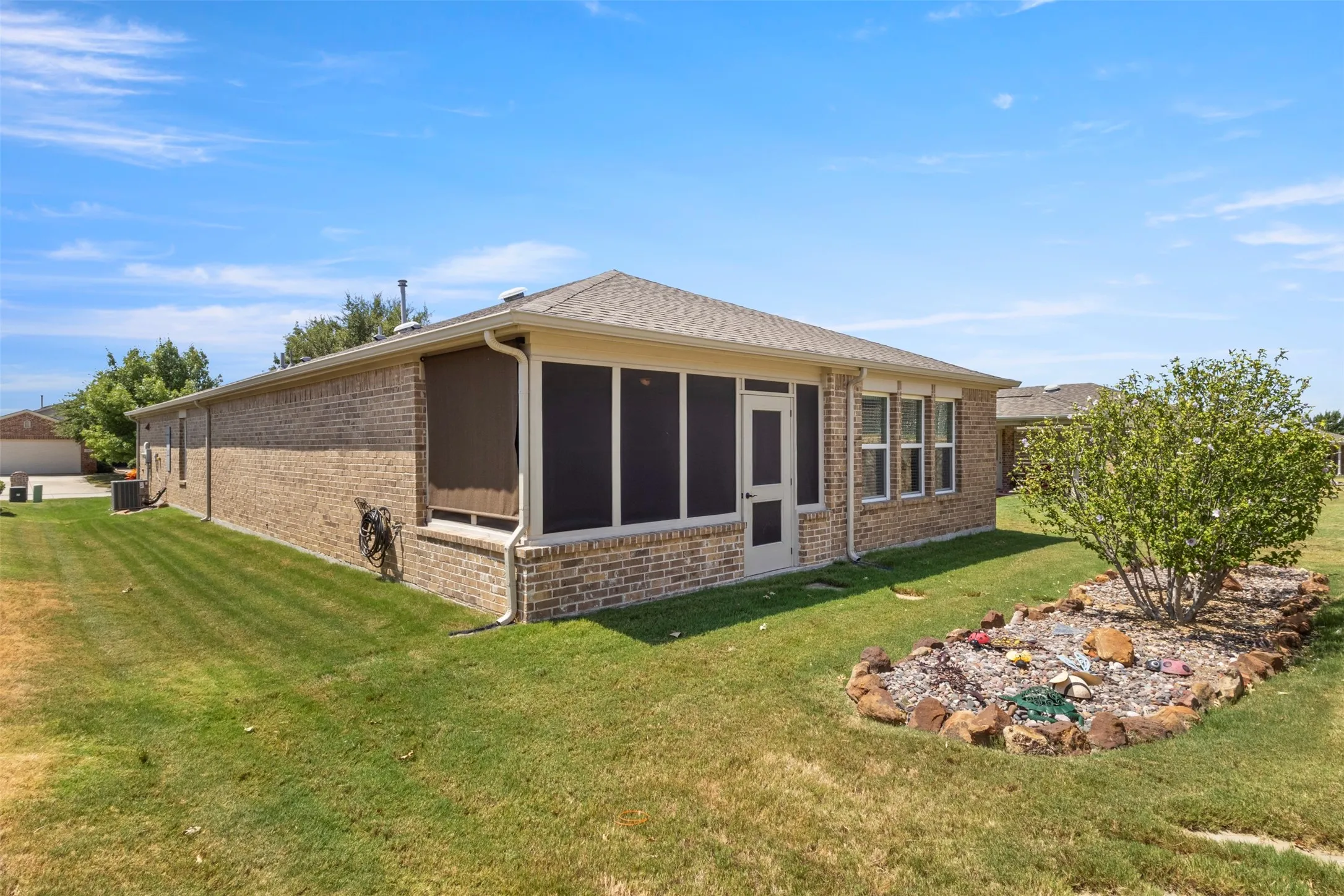 Brick exterior with a screened porch, multiple windows, and a landscaped garden bed