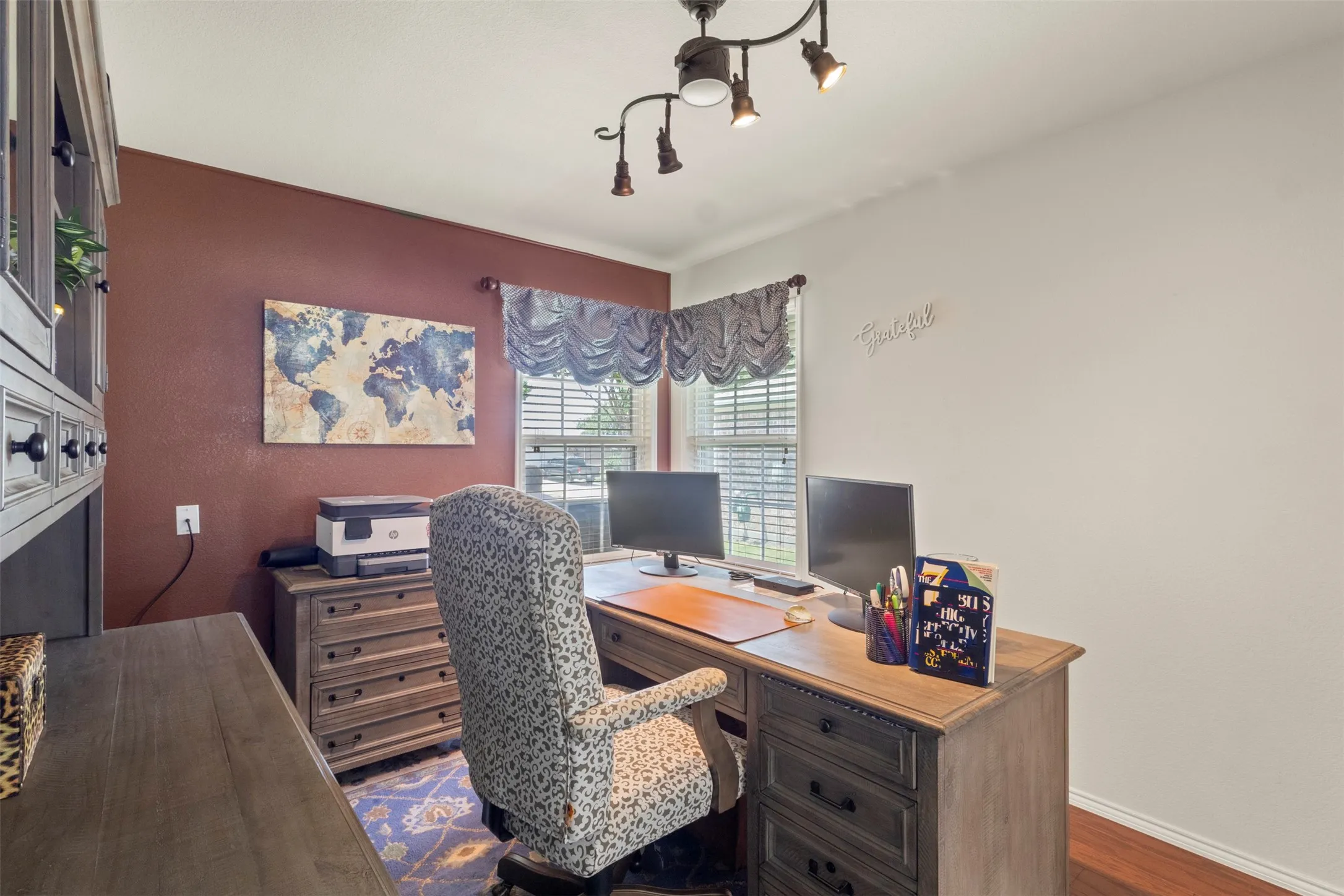 Recessed window with horizontal blinds, track lighting fixture, wood-finish flooring, and built-in cabinetry