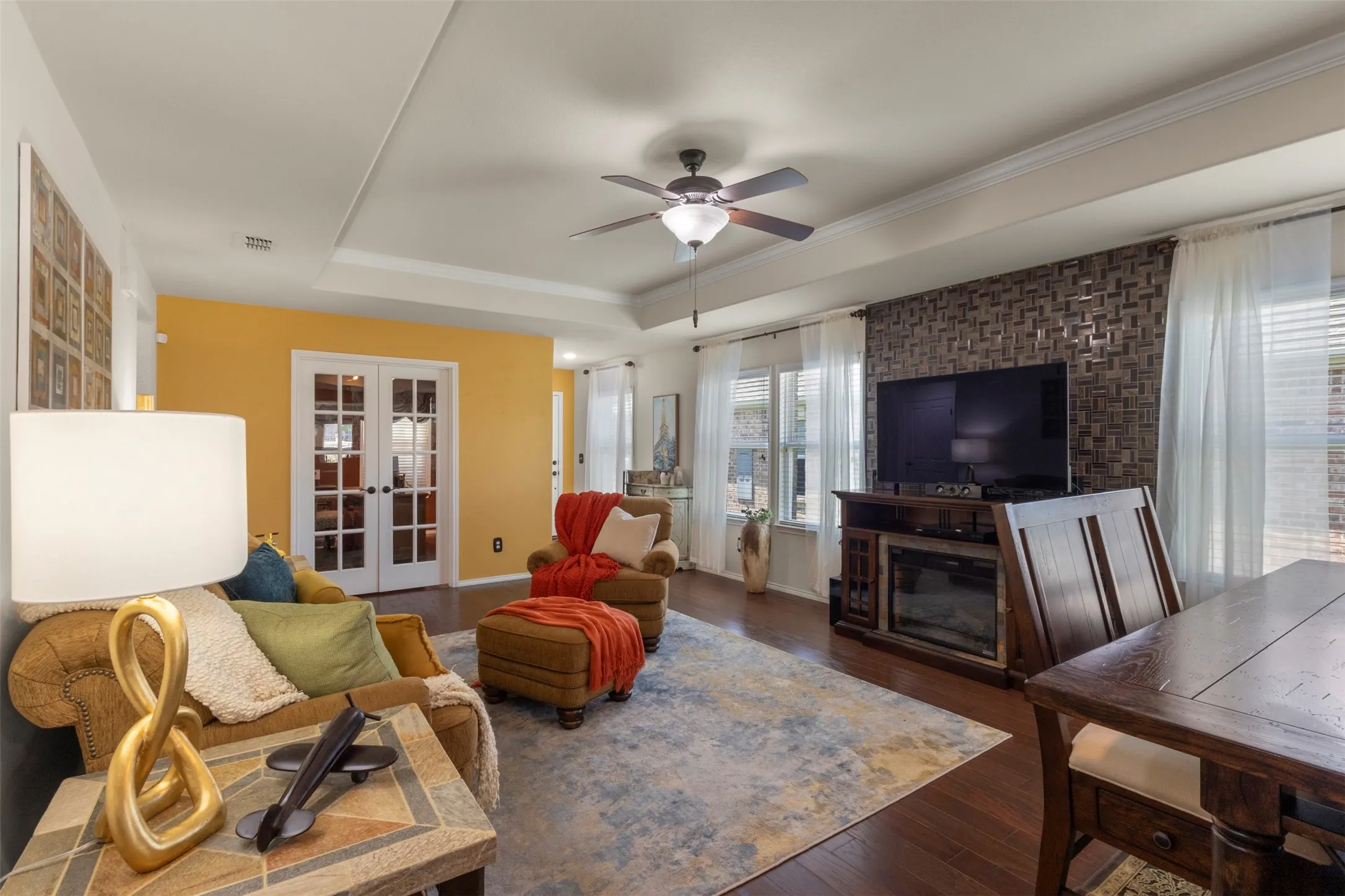 Tray ceiling with crown molding, wood-finish flooring, ceiling fan, and French doors