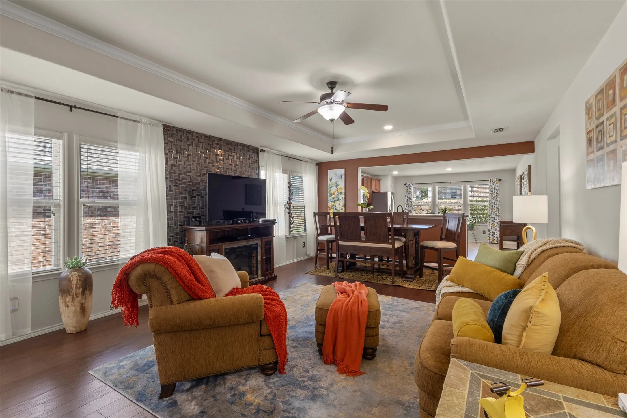 Tray ceiling with crown molding, wood-finish flooring, a decorative accent wall, recessed lighting, and a ceiling fan