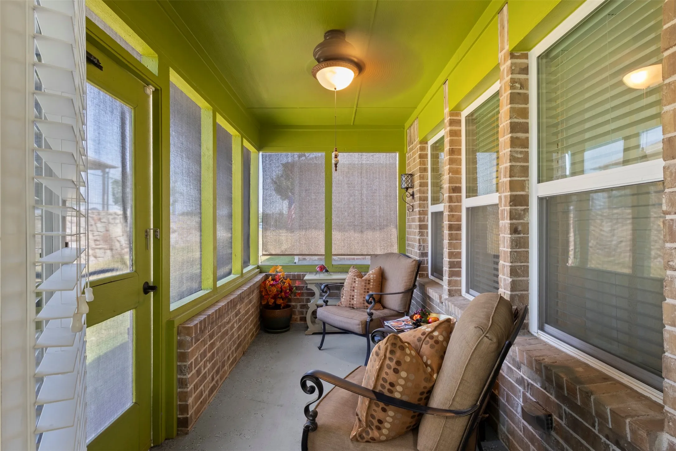 Screened porch featuring a brick half-wall, multiple windows with blinds, a ceiling-mounted light fixture, and a full-light exterior door