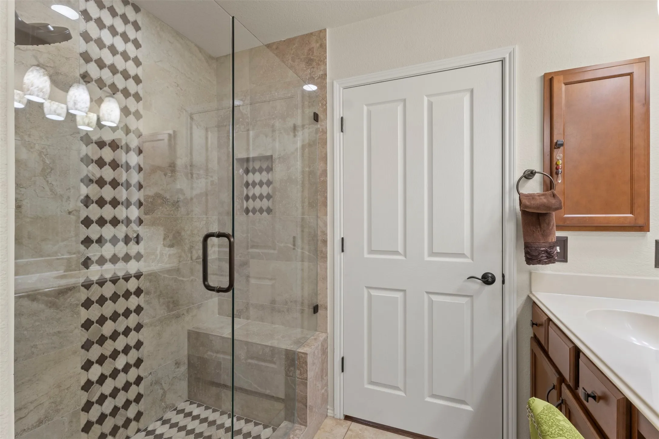 Glass-enclosed shower with a patterned tile accent wall, built-in shower bench, and dark bronze hardware