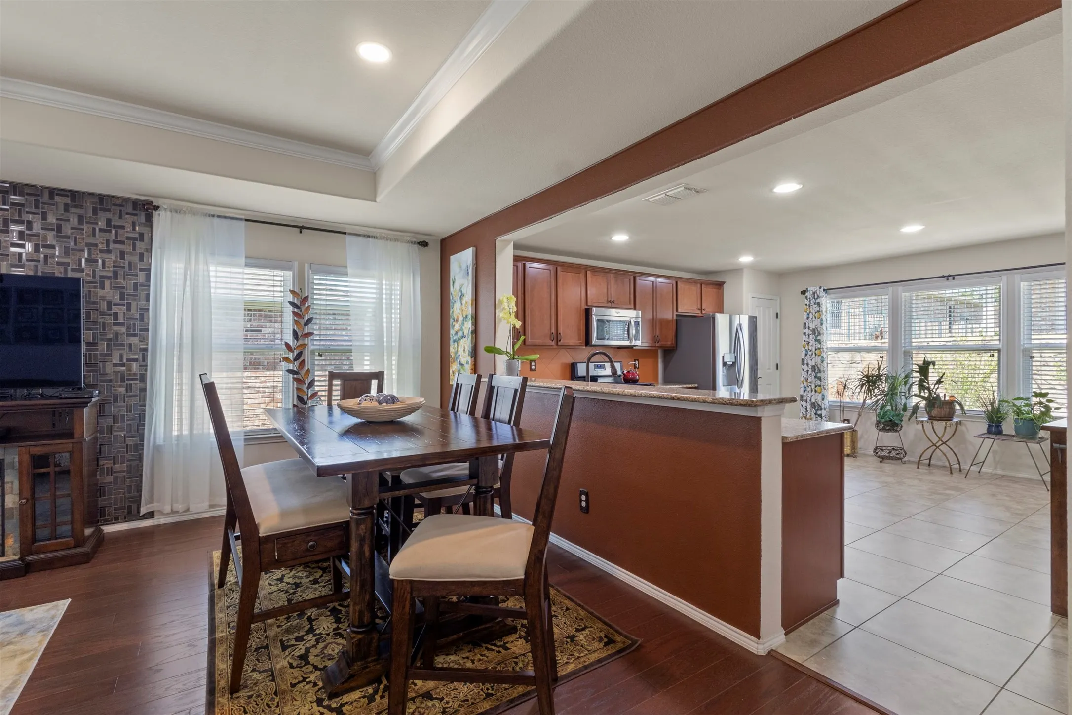 Open-concept living space with wood-finish flooring, a tray ceiling, recessed lighting, and kitchen with wood cabinetry and stainless steel appliances