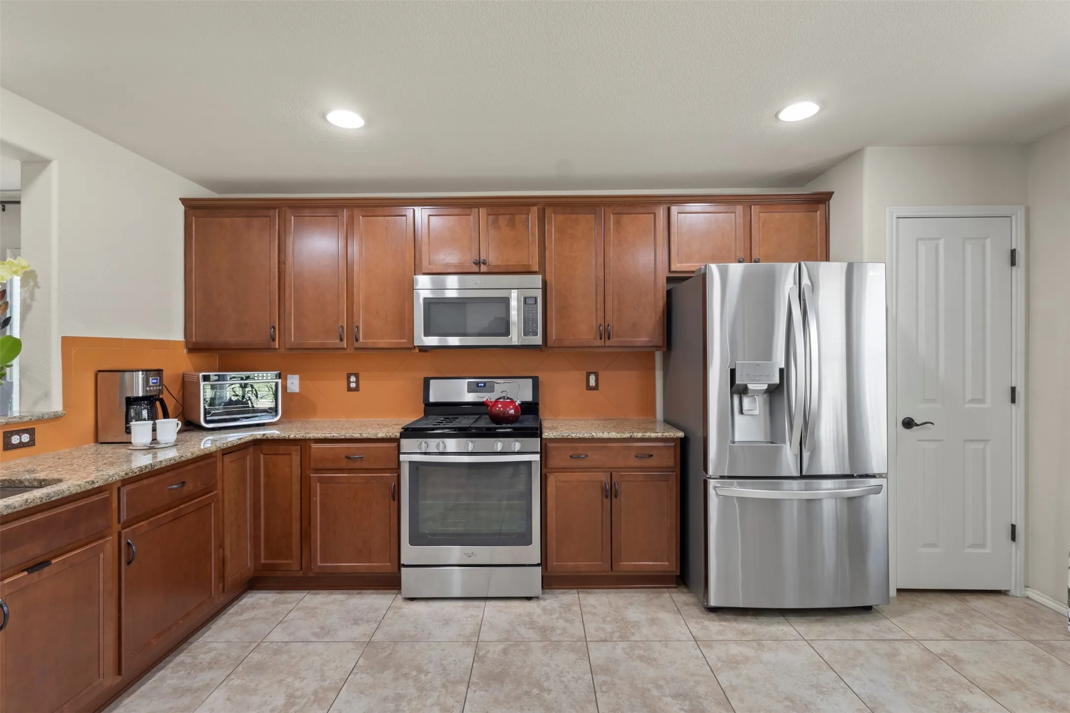 Kitchen featuring wood cabinetry, stainless steel appliances, speckled countertops, and tile flooring