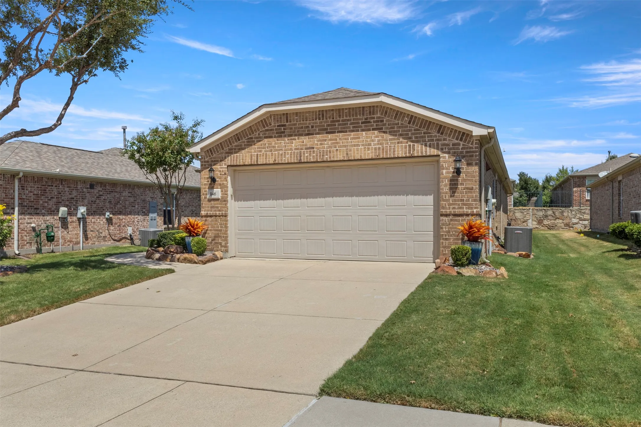 Brick exterior with an attached garage, concrete driveway, and established landscaping