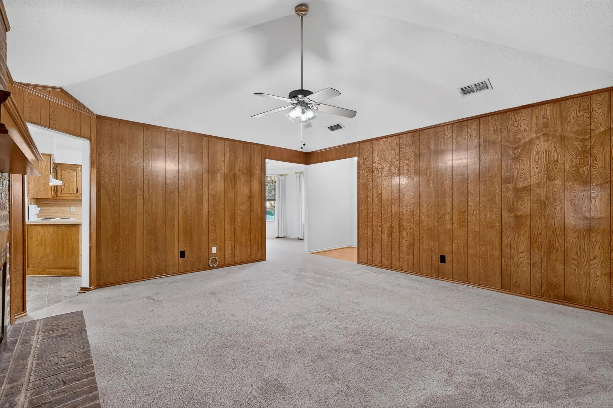 Vaulted ceiling with a ceiling fan, wood-paneled walls, and carpet flooring