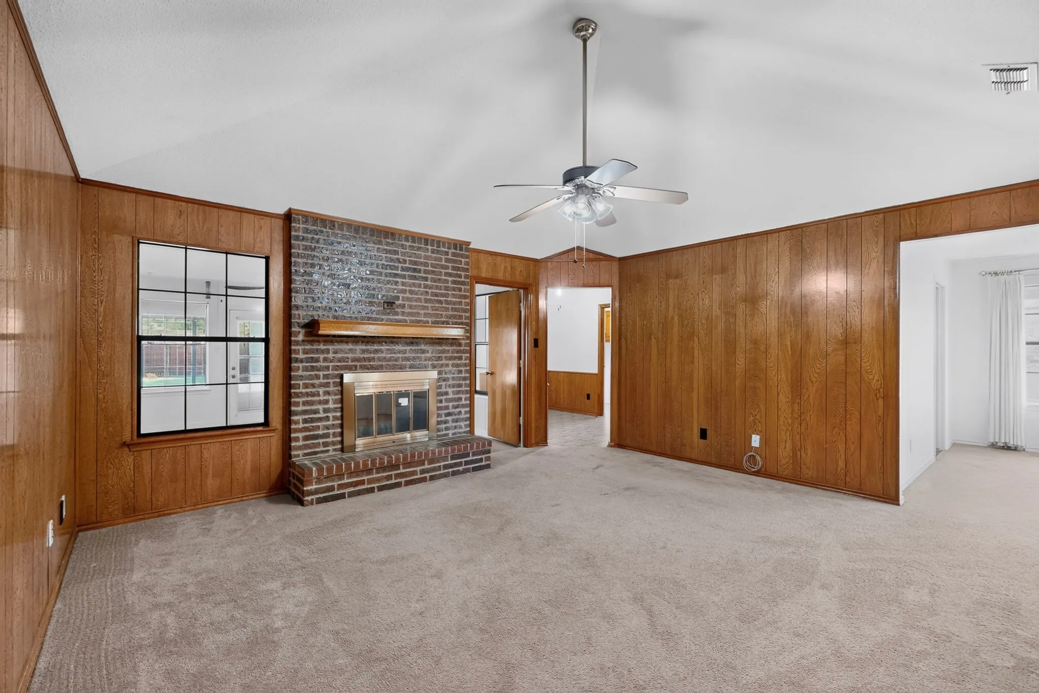 Brick fireplace with a wood-finish mantel, vaulted ceiling, ceiling fan, and wood-paneled walls