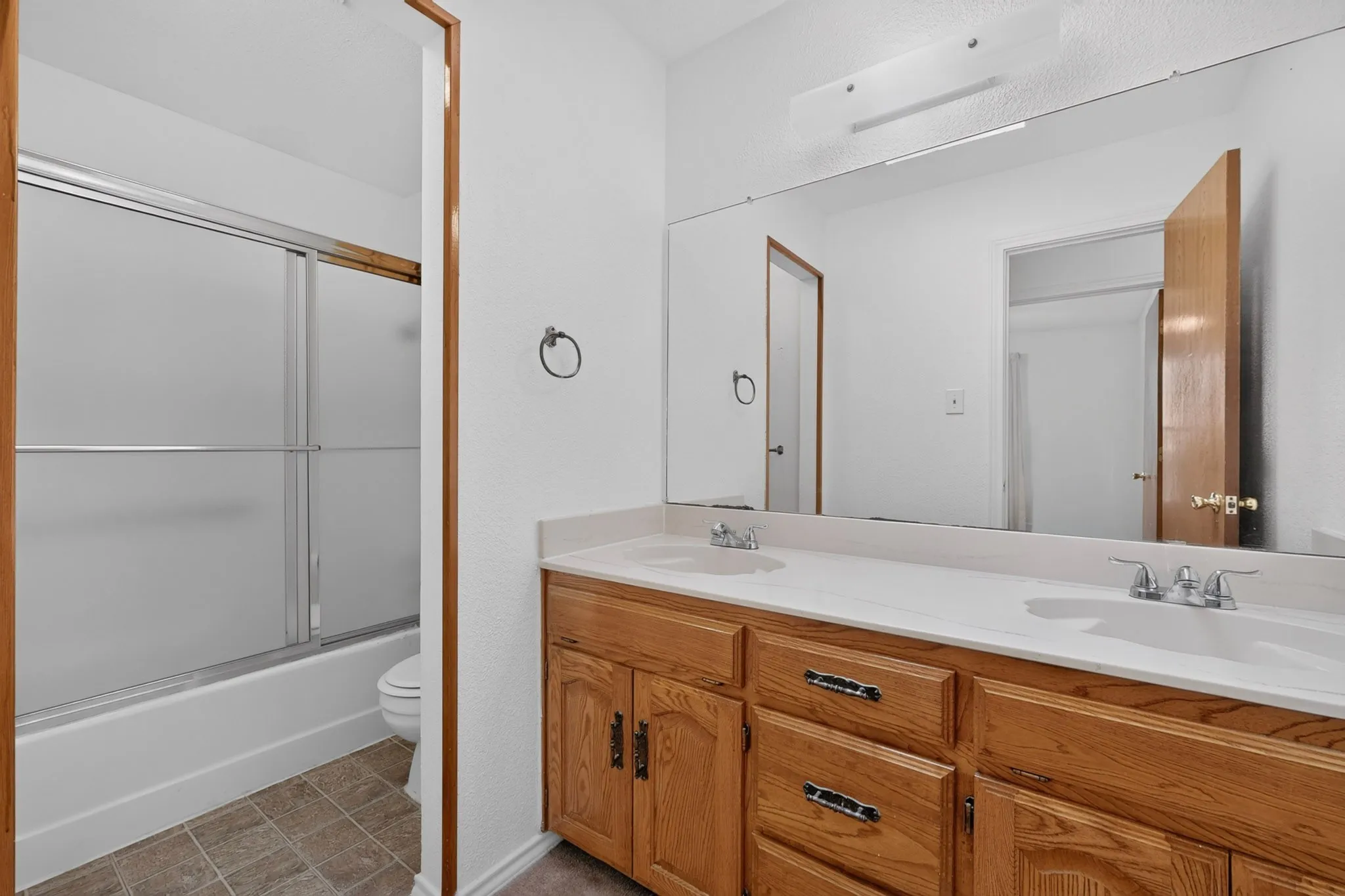 Double vanity with dual sinks, warm wood-finish cabinetry, and a large wall-mounted mirror