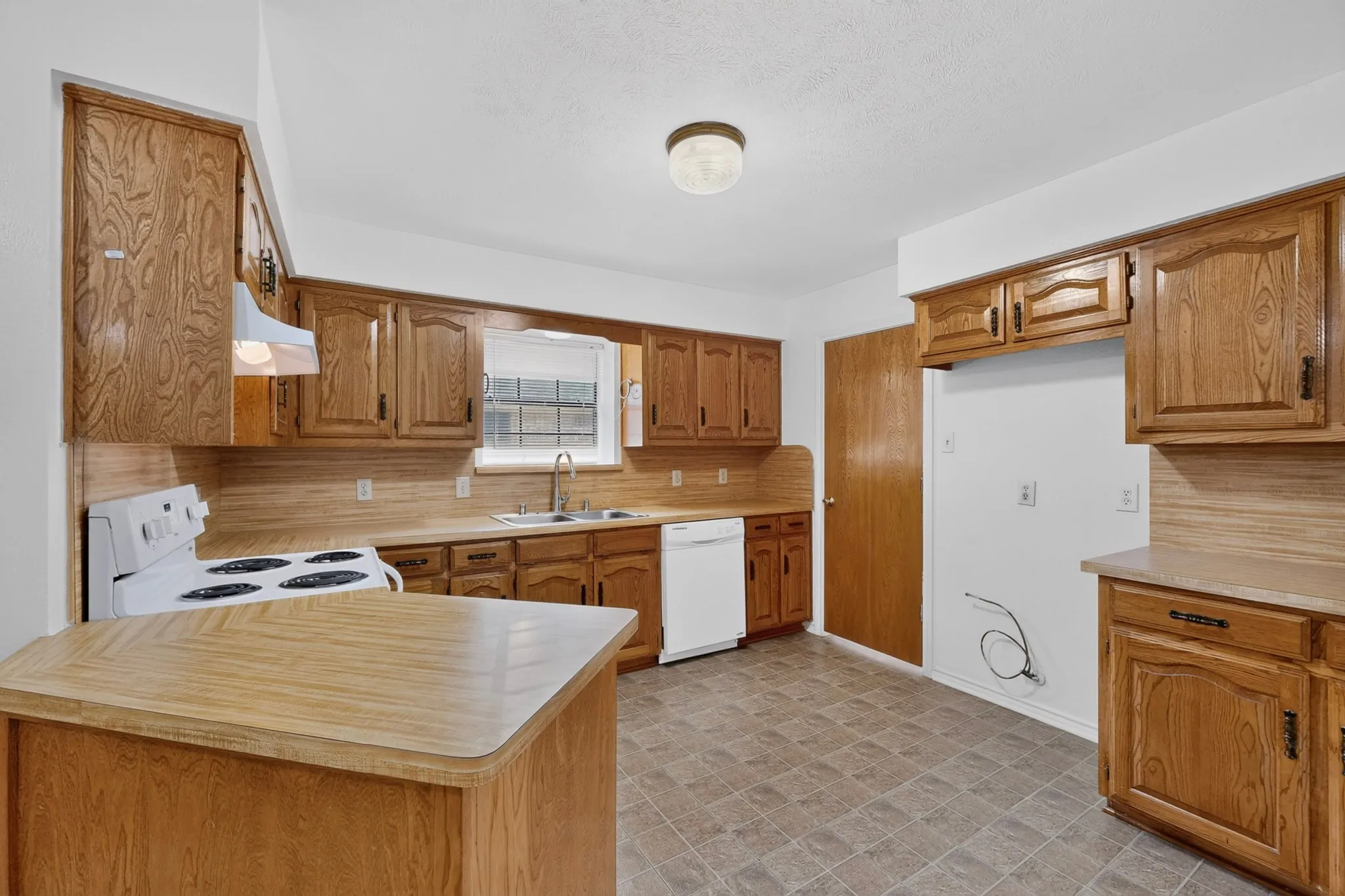 Kitchen featuring extensive wood cabinetry, a white electric range, a stainless steel sink, a white dishwasher, and durable tile flooring