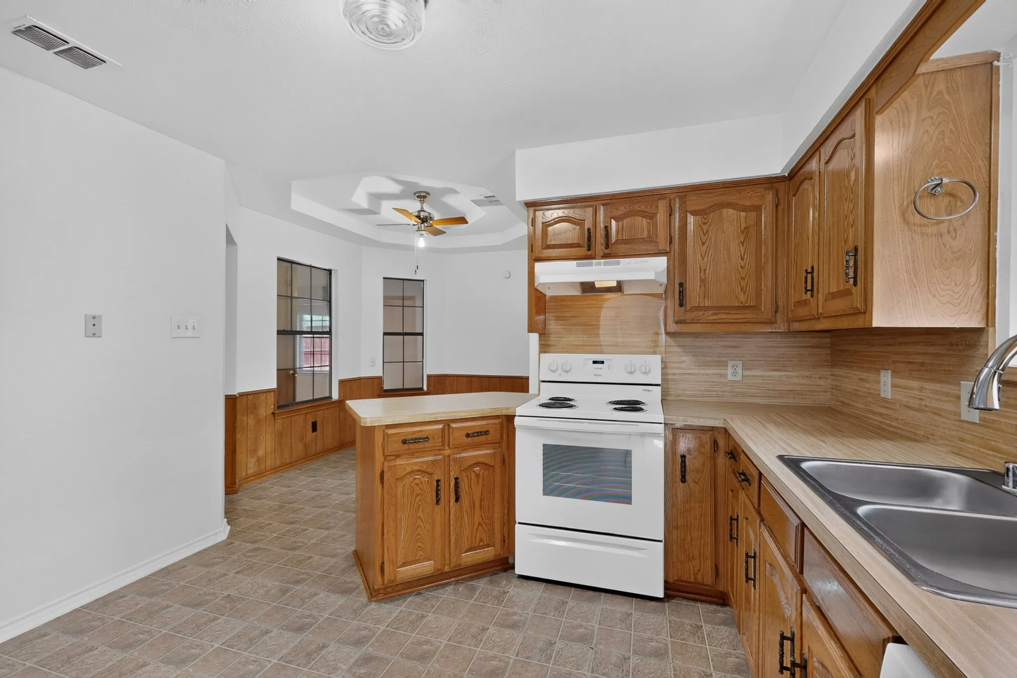 Kitchen featuring wood cabinetry, white electric range, double basin stainless steel sink, and light-toned countertops