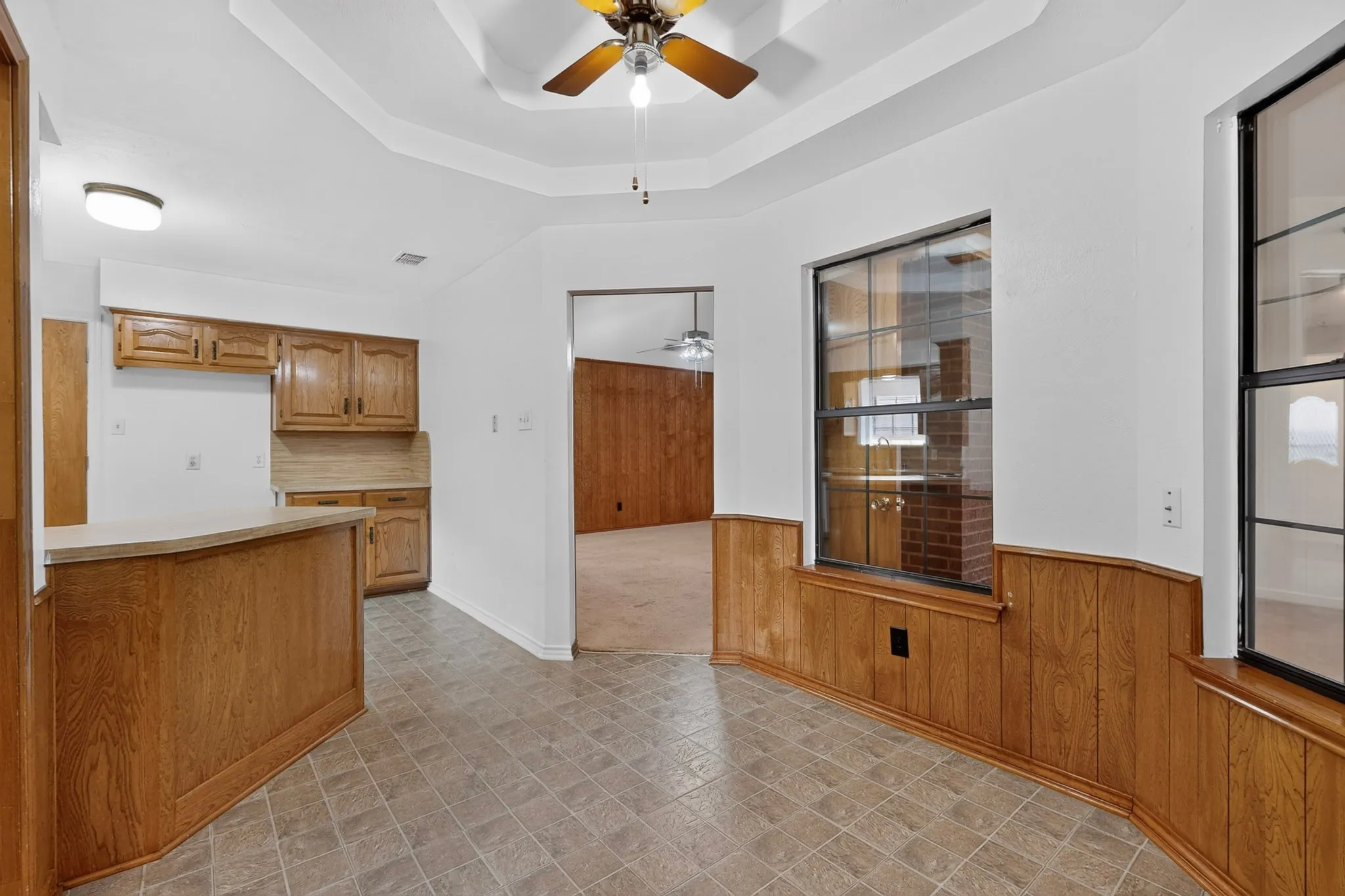 Tray ceiling with a ceiling fan, wood-finish kitchen cabinetry, breakfast bar, and wood paneling