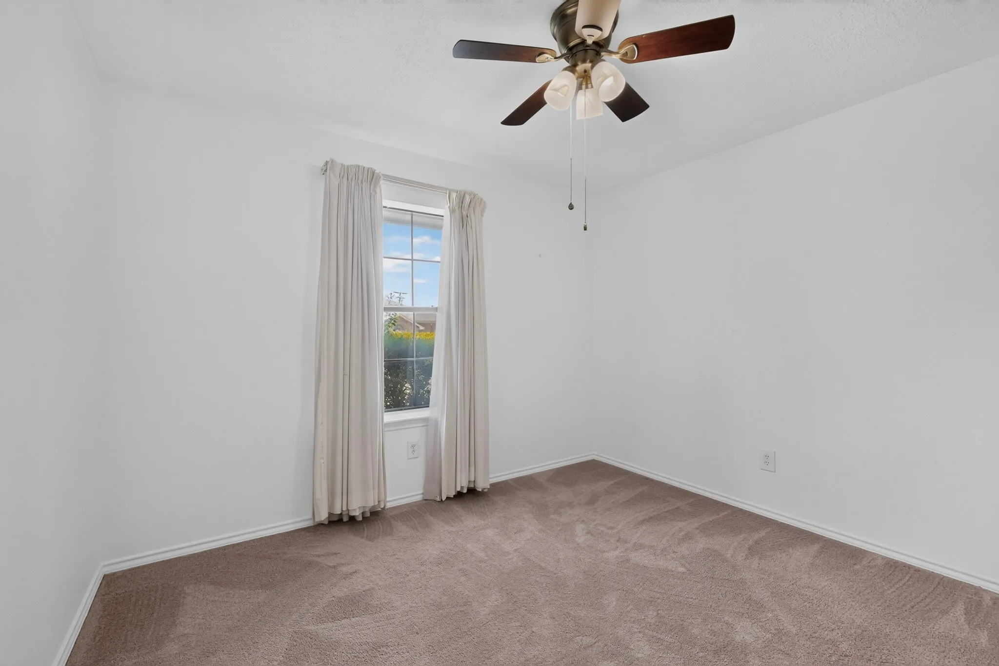 Bright bedroom showcasing neutral carpet flooring, ceiling fan with integrated lighting fixture, and a glass door opening to natural outdoor light