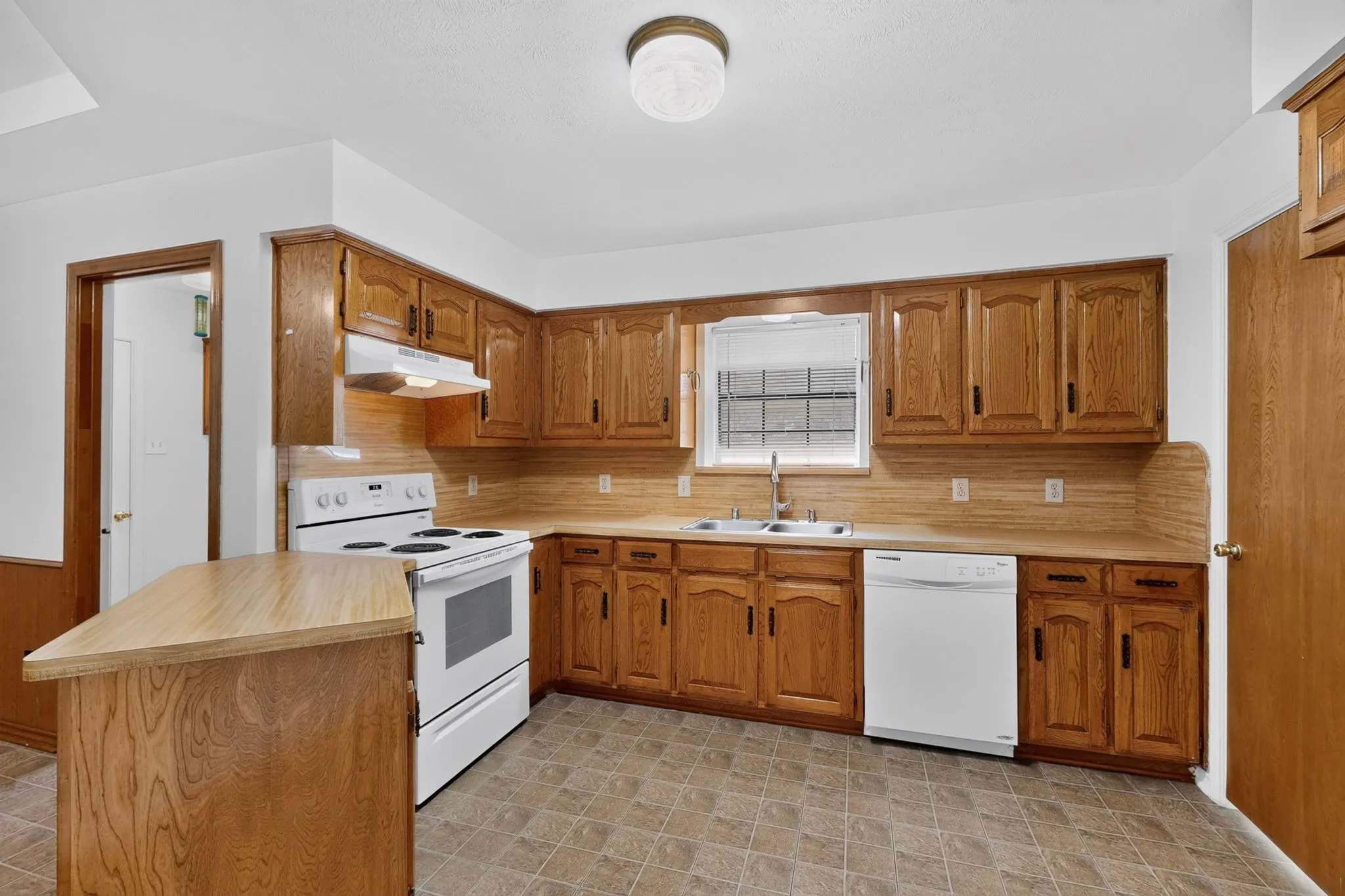Kitchen featuring wood-finish cabinetry, a double basin sink, a built-in dishwasher, and a white electric range with an overhead exhaust hood