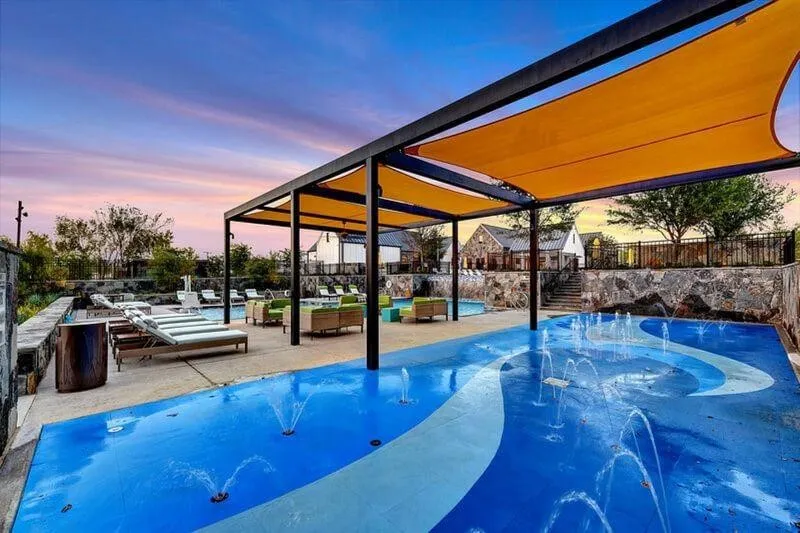 Shaded splash pad with multiple water features, expansive pool deck, and structured shade canopies