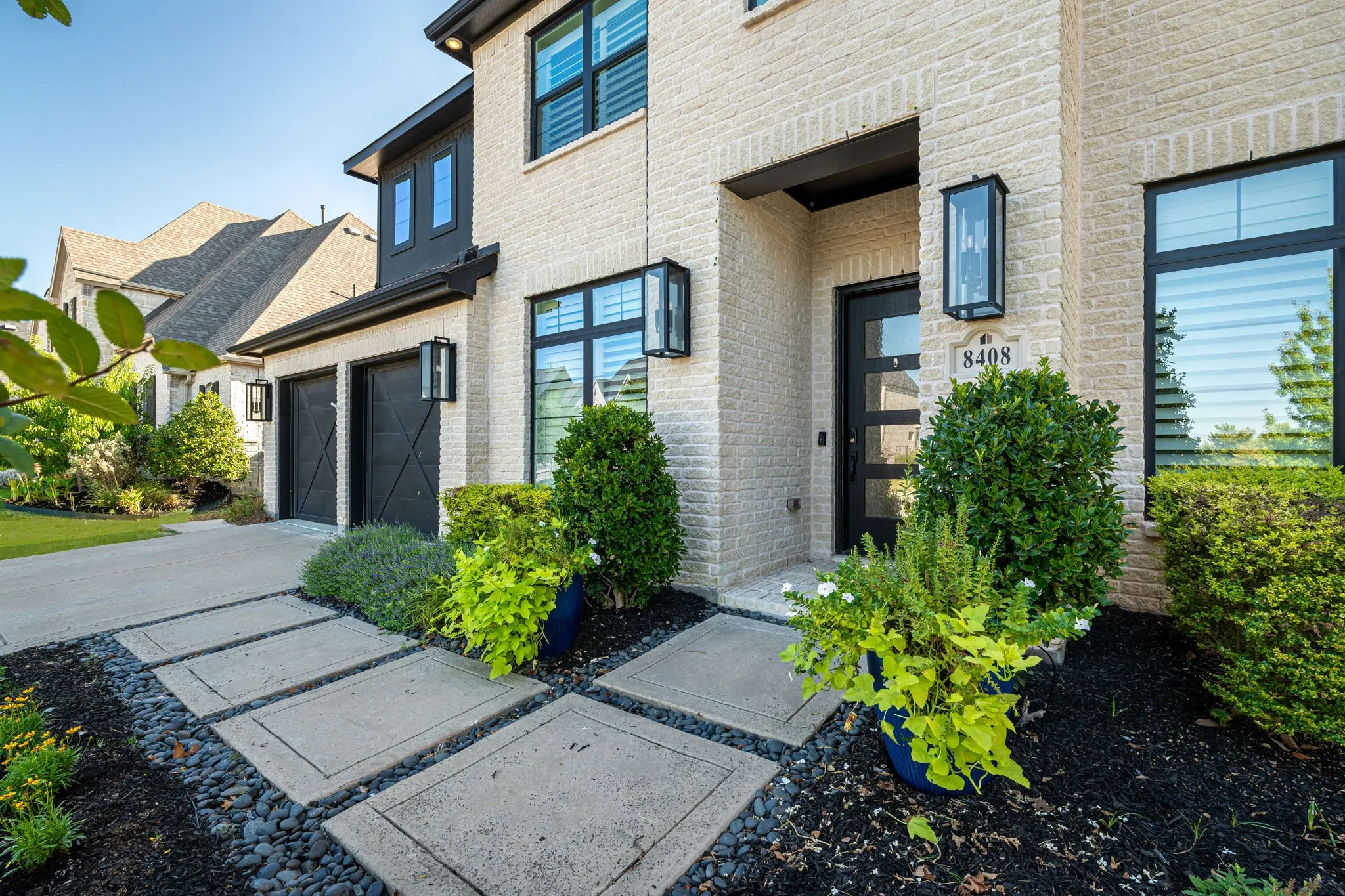 Light-colored brick facade with dark window frames, a contemporary front entry door, and a paver walkway
