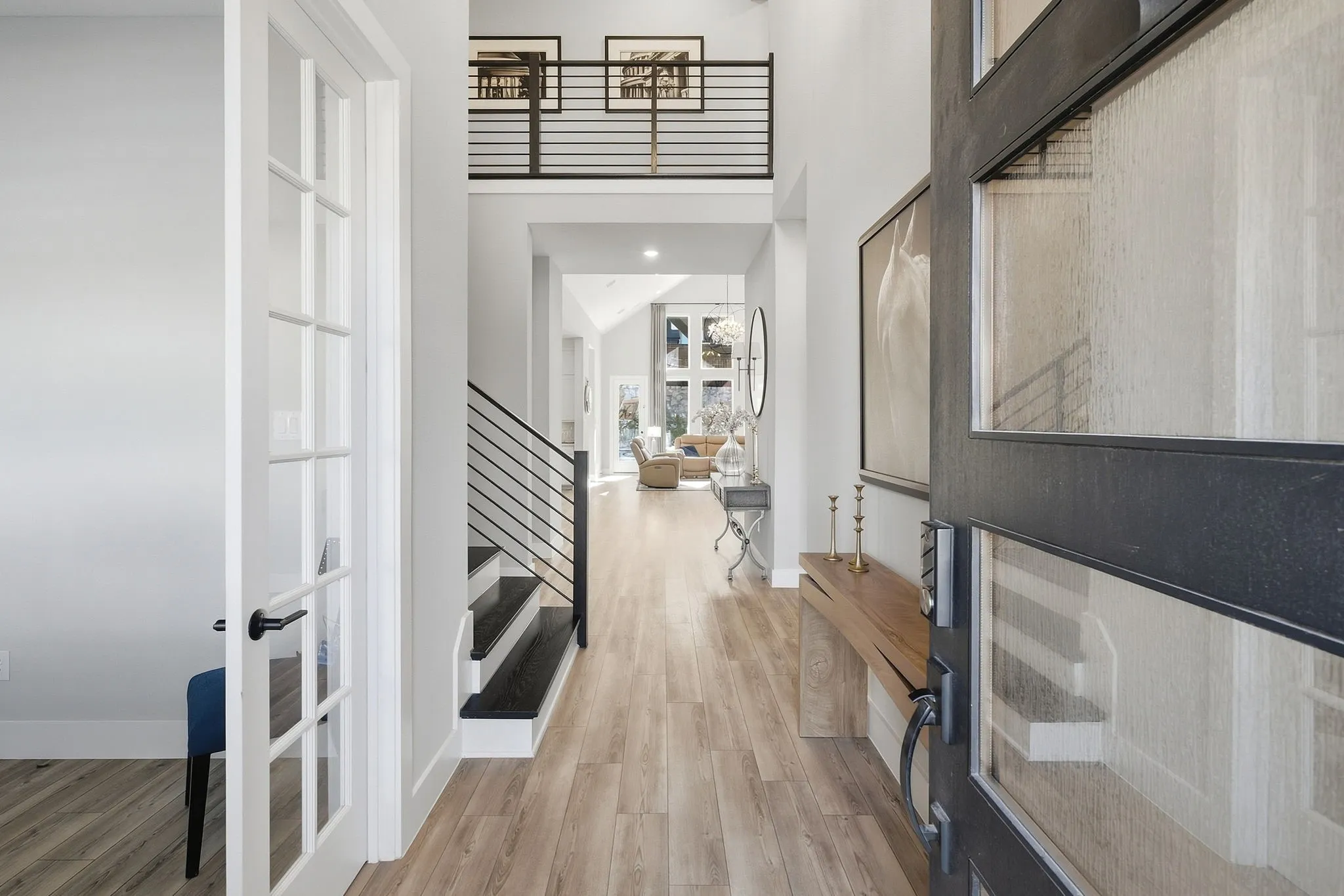 Two-story entryway featuring a black frame front door with textured glass, wood-finish flooring, a contemporary staircase with horizontal metal railings, and a second-level open hallway with matching railings