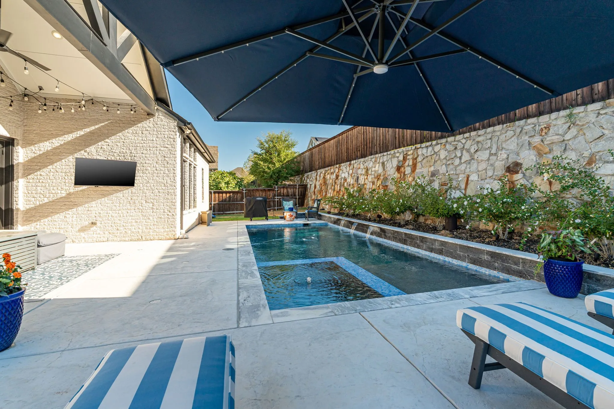 Private backyard featuring a swimming pool with integrated spa, stone privacy wall, and mature landscaping