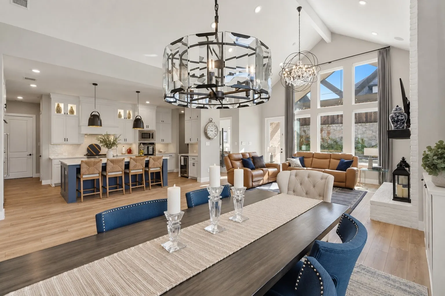 Open-concept living area featuring a vaulted ceiling with exposed beams, wood-finish flooring, and a white brick fireplace