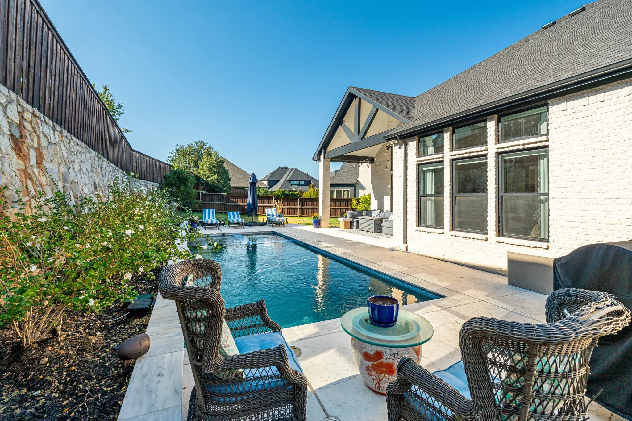 Private backyard featuring a pool with water features, stone retaining wall, mature landscaping, and a covered patio