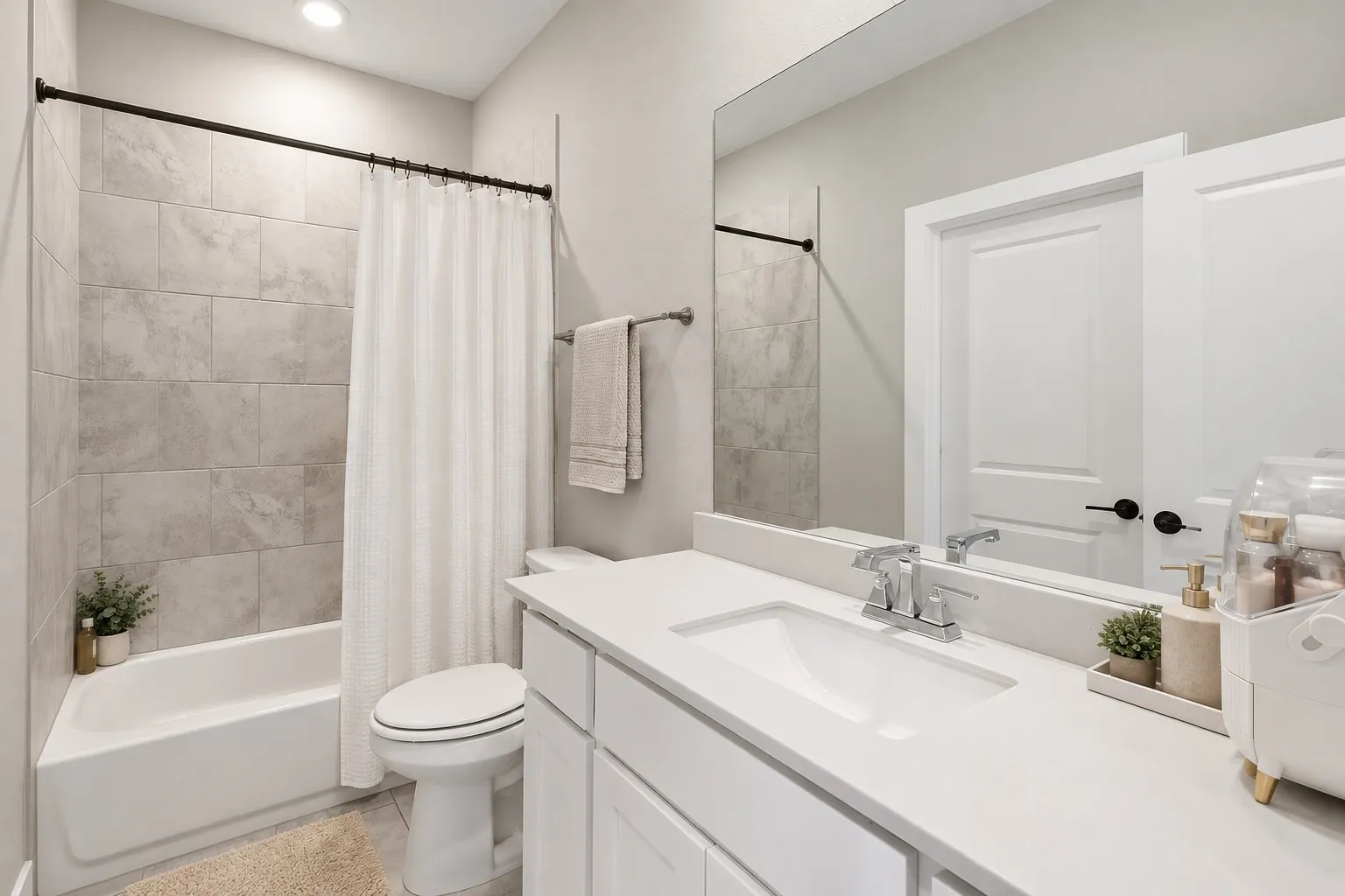 White vanity with an integrated sink and chrome faucet, large mirror, white bathtub with tiled surround, and recessed lighting