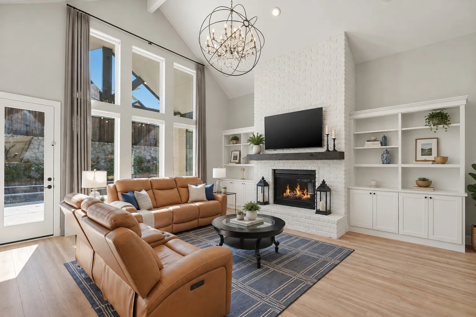 Vaulted ceiling with a chandelier, floor-to-ceiling windows, white brick fireplace with a dark wood mantel, built-in shelving, and wood-finish flooring