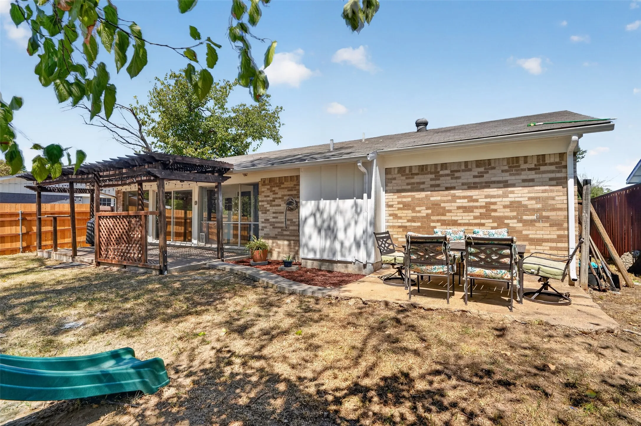 Brick exterior with a covered patio area, concrete patio, and a wooden fence