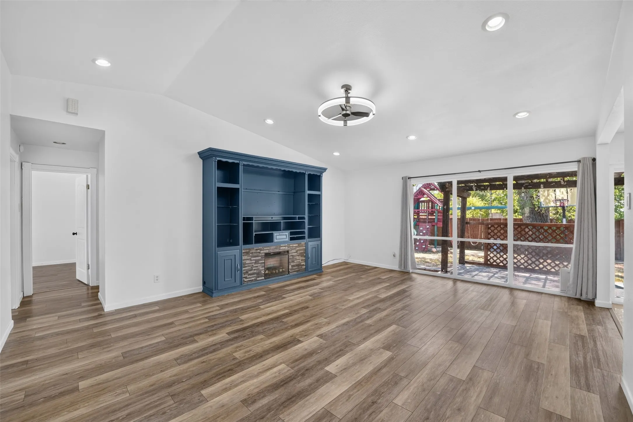 Vaulted ceiling, recessed lighting, wood-finish flooring, built-in entertainment center with stone accent, and sliding glass doors