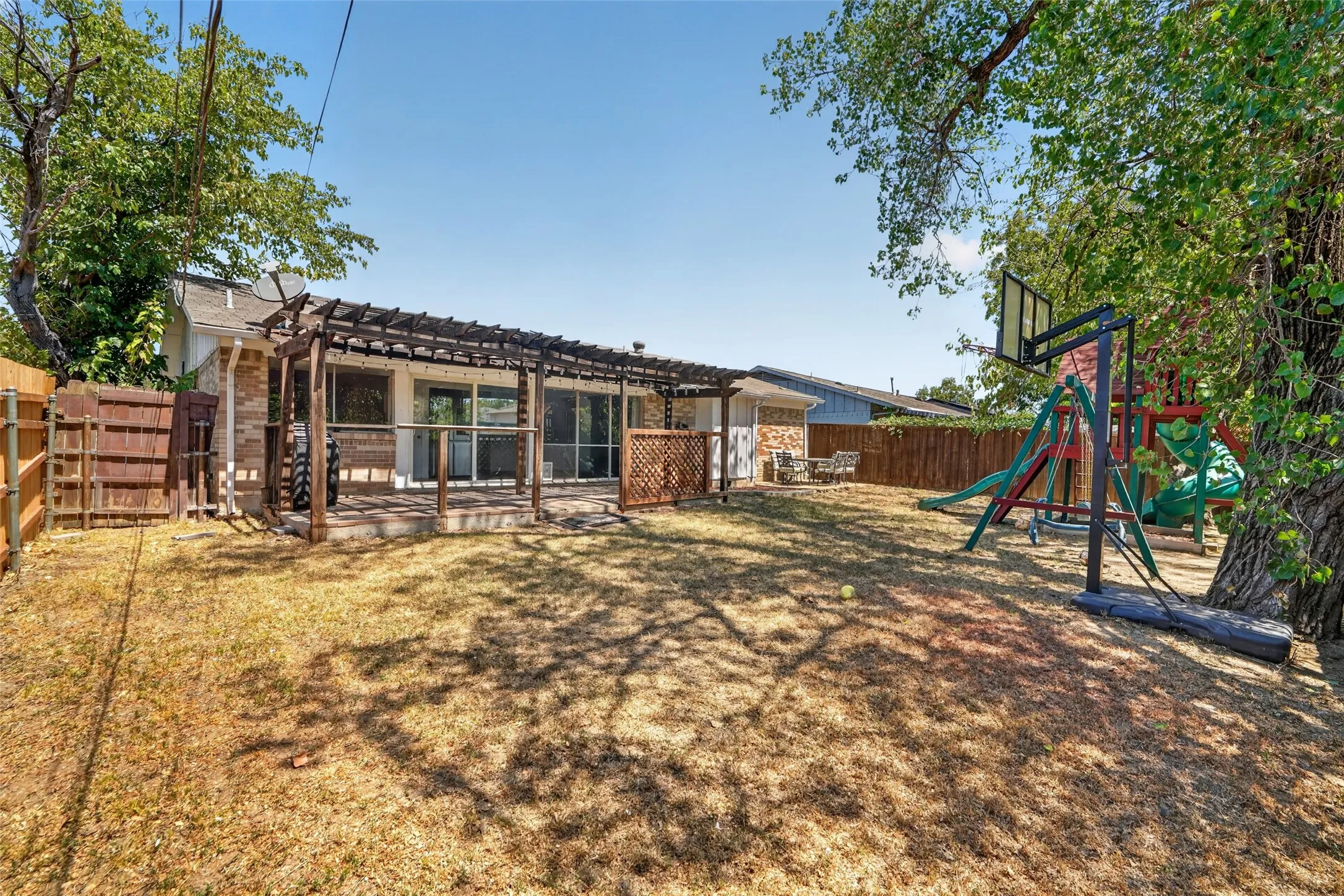 Expansive backyard featuring a wood privacy fence, mature trees, and a pergola-covered patio