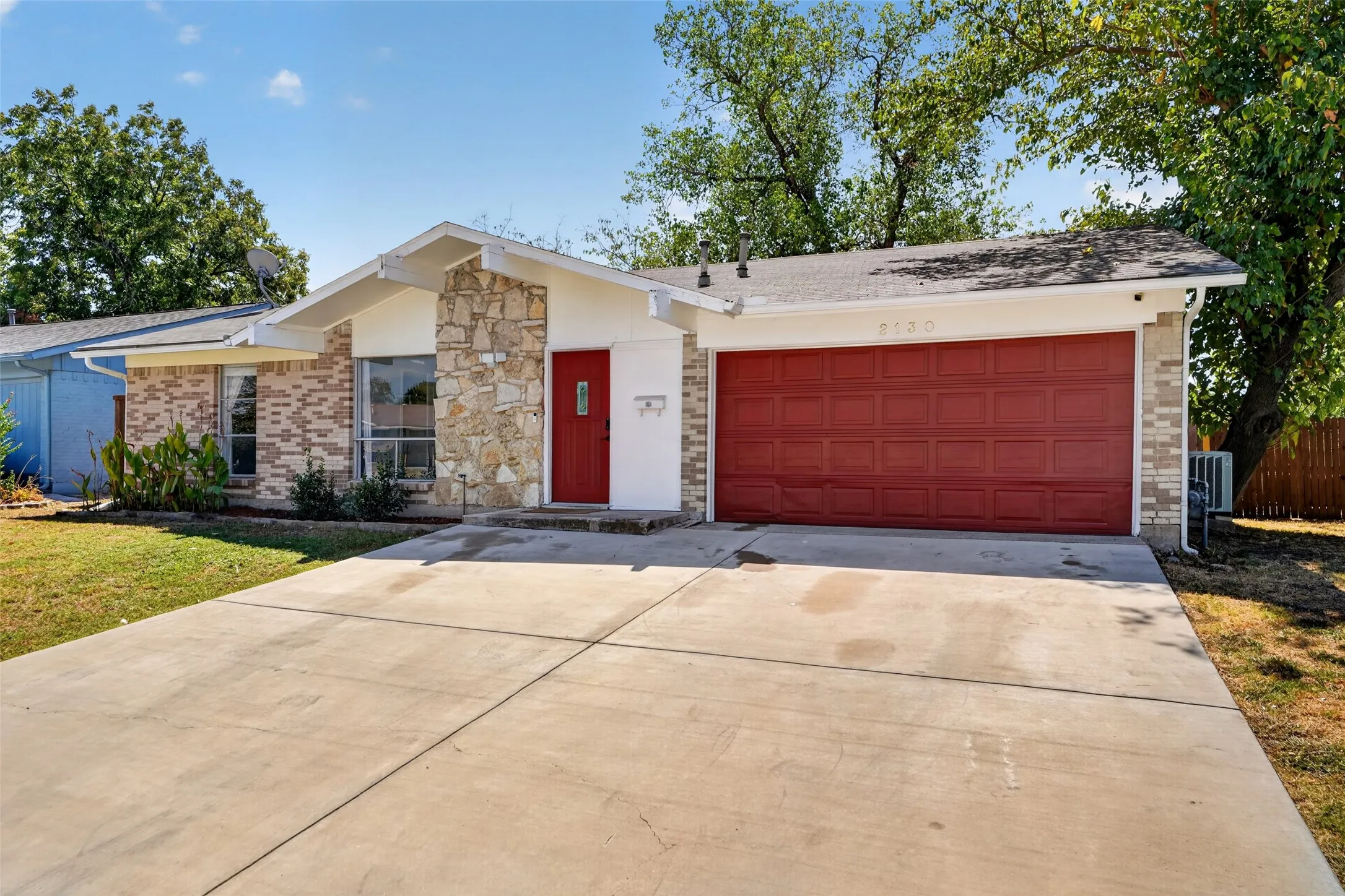 Exterior featuring brick and stone veneer, a red front door, a red garage door, and a concrete driveway