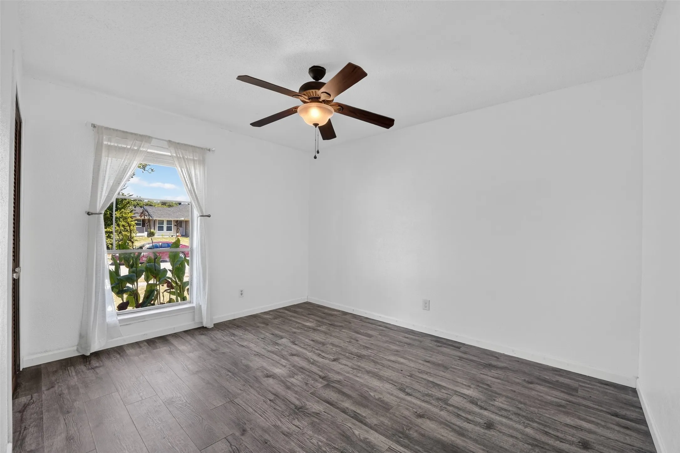 Wood-finish flooring, a window with natural light, and a ceiling fan with integrated lighting