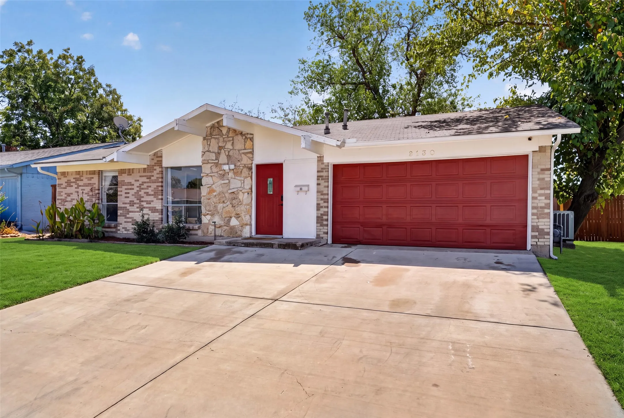 Stone and brick facade with a red entry door, a red garage door, and a concrete driveway