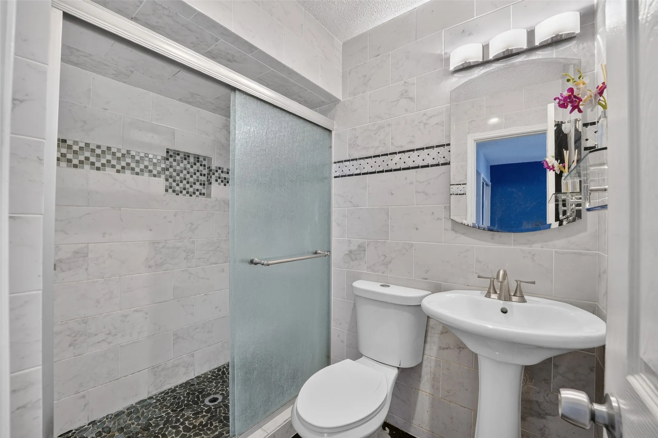 Shower with sliding glass enclosure, mosaic tile accent, and pebble-finish floor