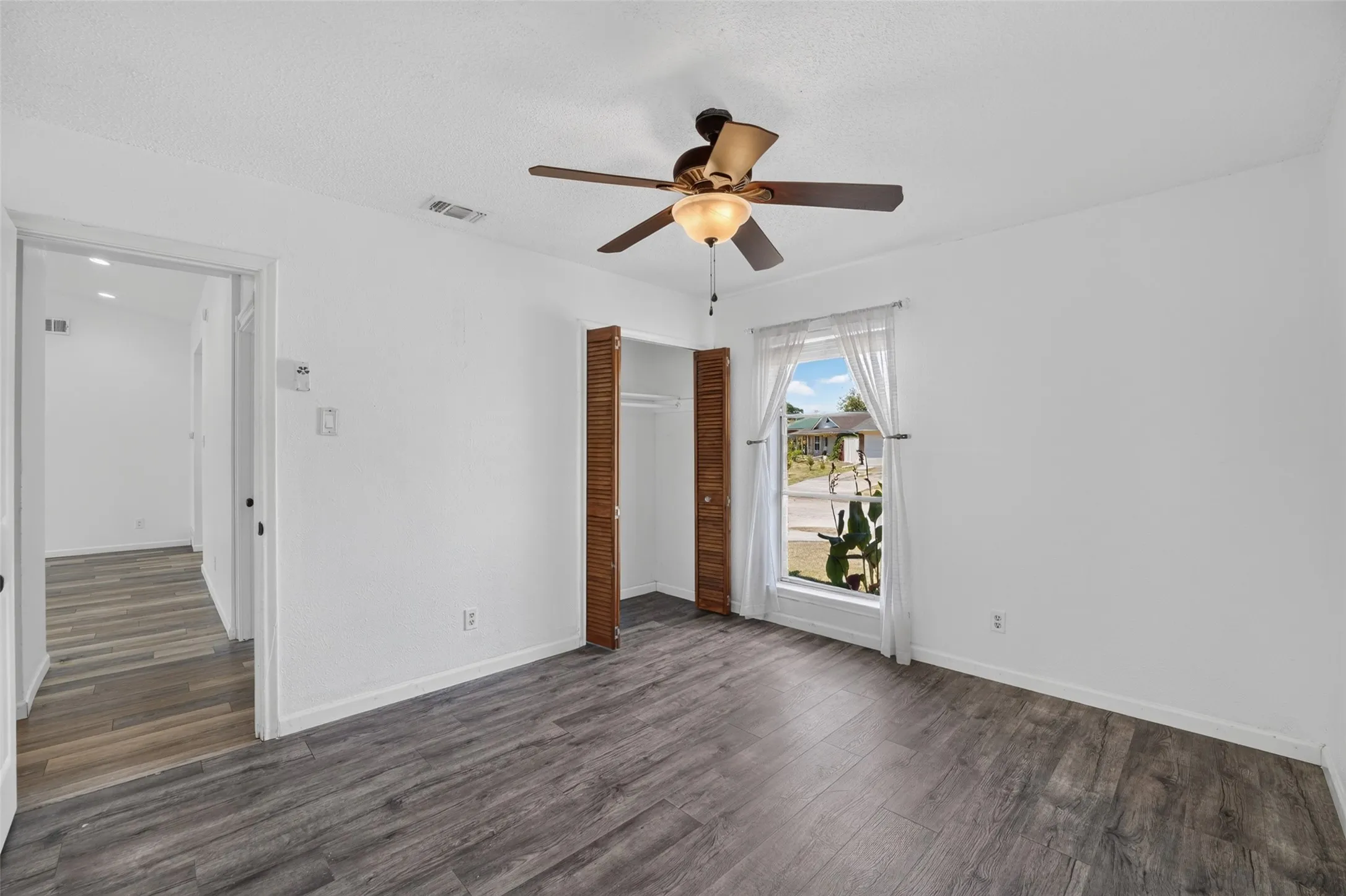 Wood-finish flooring throughout, bright window with natural light, integrated ceiling fan with lighting, and bi-fold closet doors