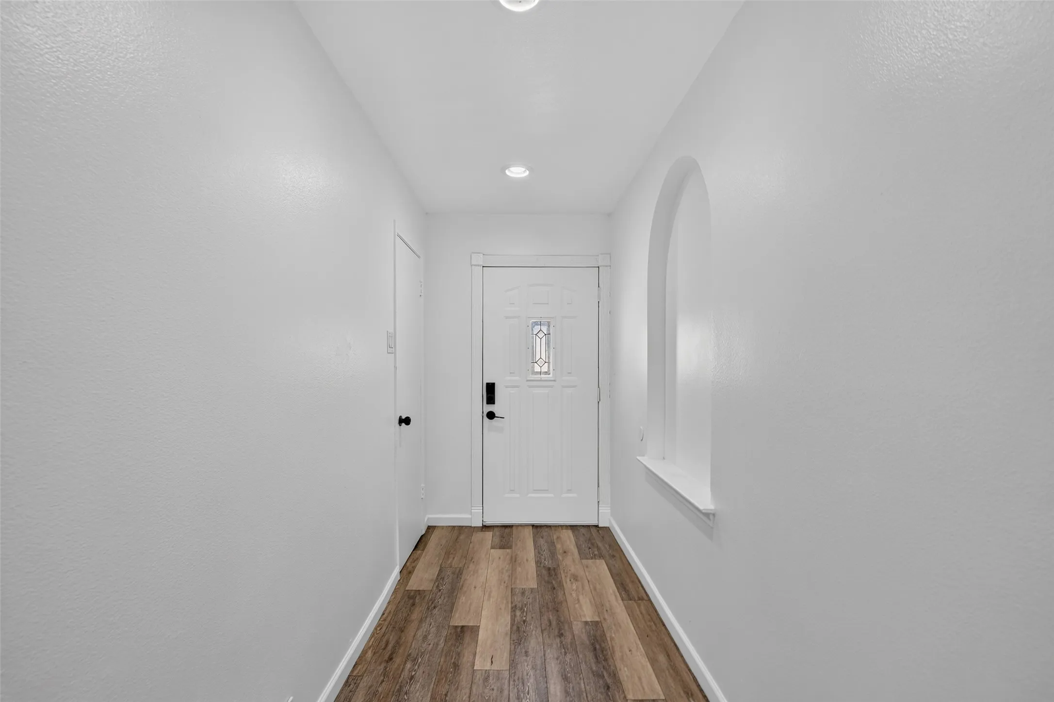 Entryway featuring wood-finish flooring, recessed lighting, an arched niche, and a white paneled door with decorative glass