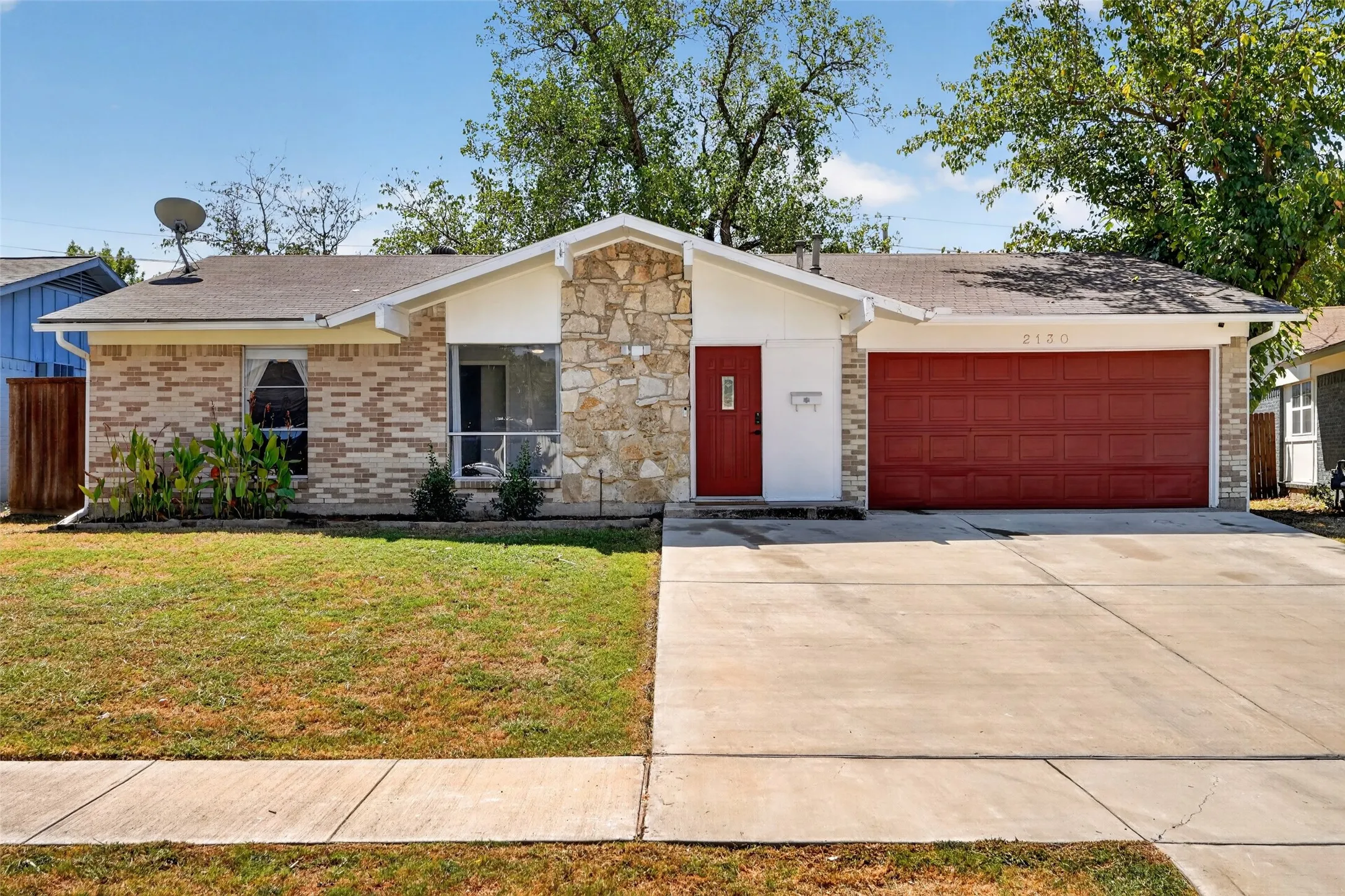 Brick and stone exterior featuring a red entry door, a red garage door, and a concrete driveway