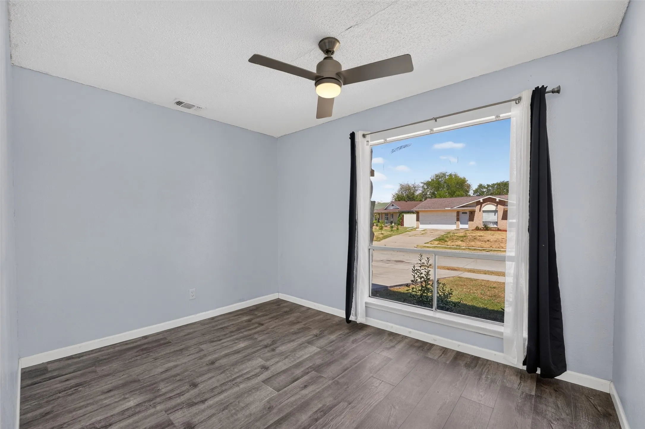 Wood-finish flooring, a ceiling fan with integrated lighting, and a large window with white trim