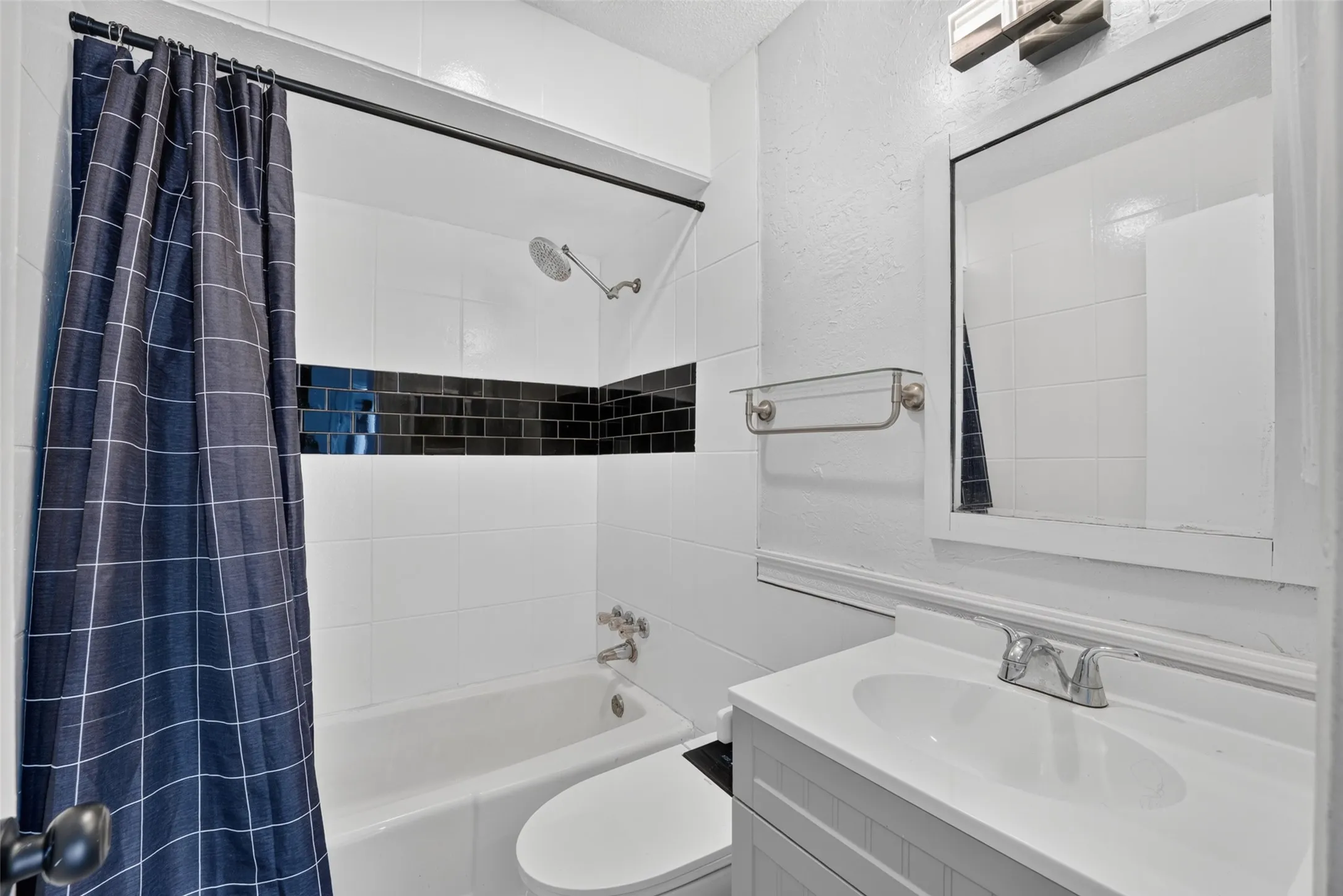 Bathroom featuring a vanity with an integrated sink, a framed mirror, and a bathtub with white and black subway tile surround