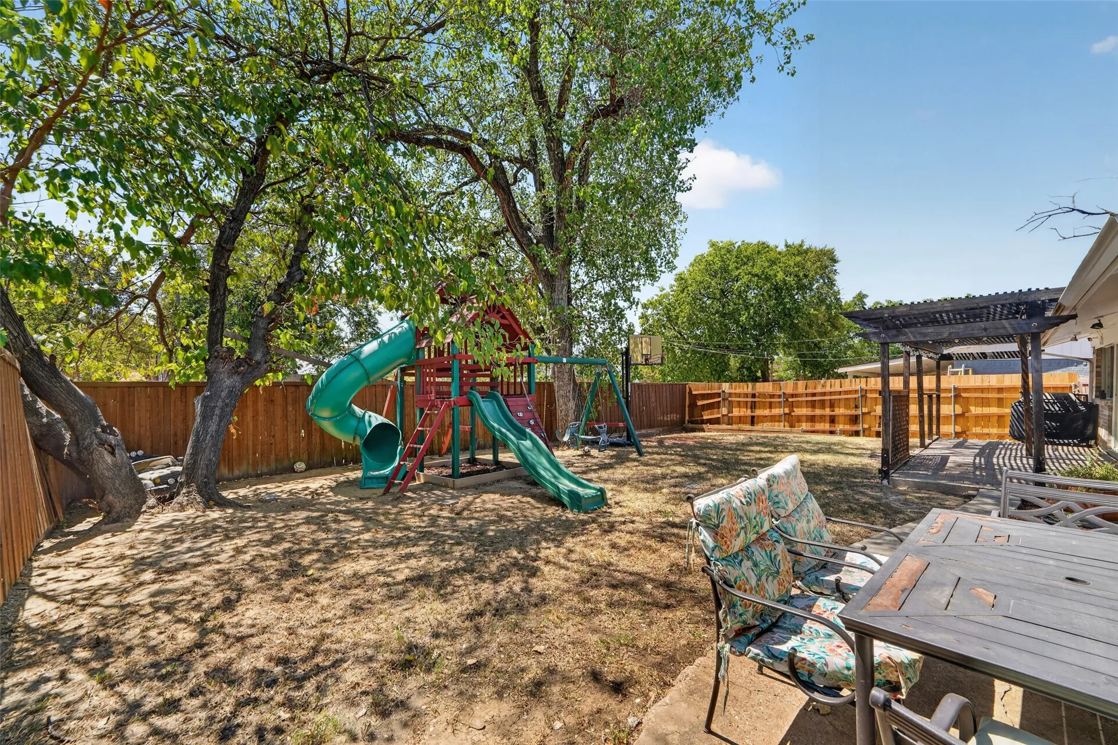 Expansive backyard featuring mature trees, a wood privacy fence, and an attached concrete patio with a dark-finish pergola