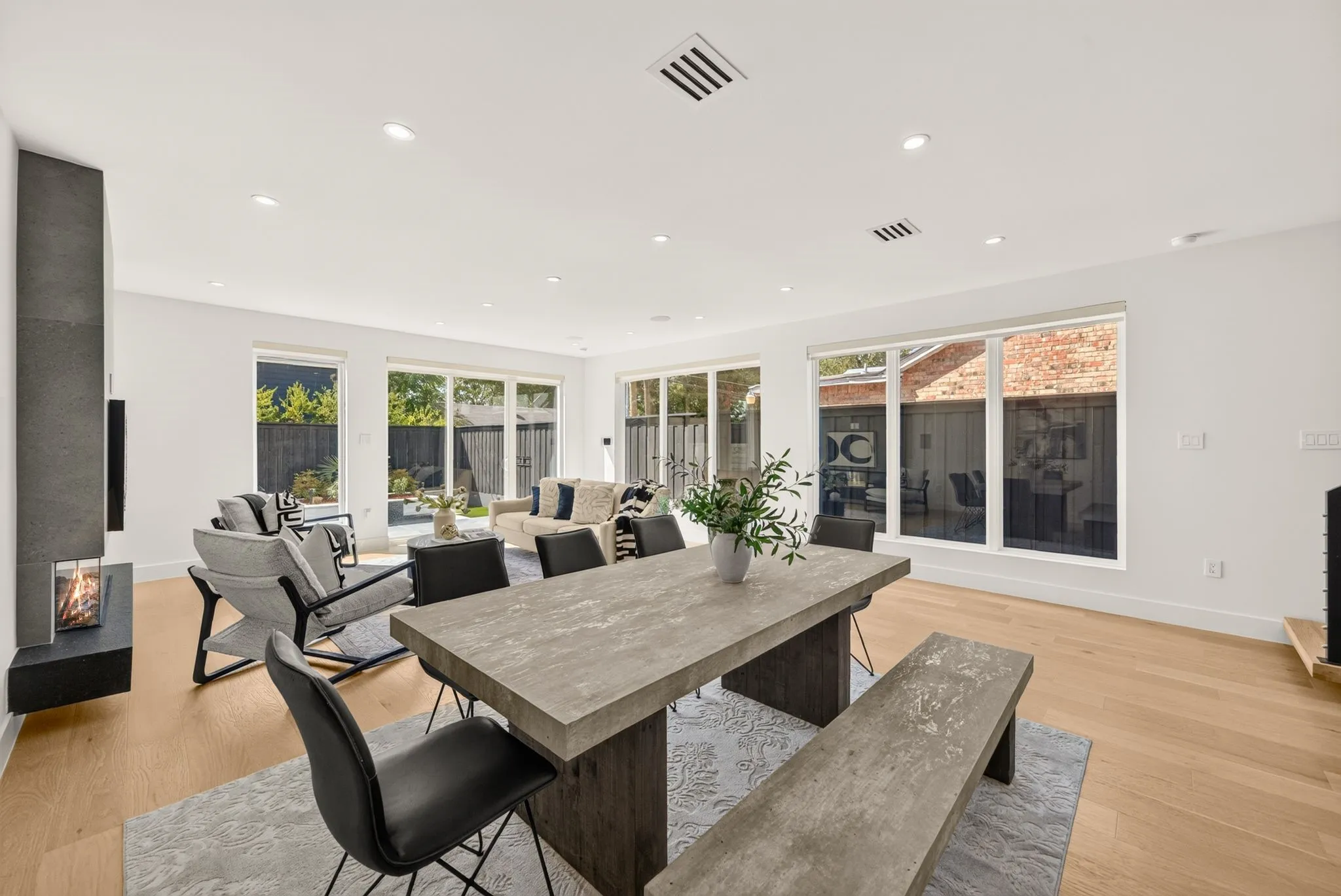 Open-concept living area with light wood-finish flooring, a contemporary fireplace, recessed lighting, and multiple large windows