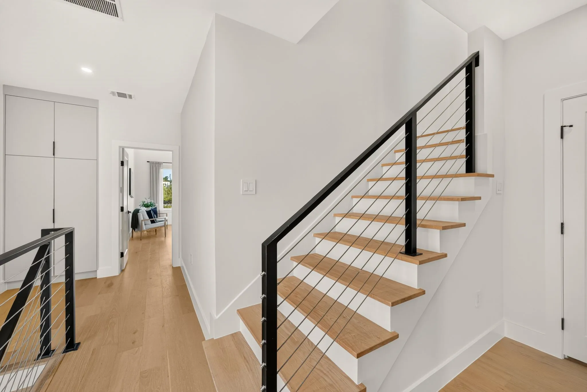Wood-finish flooring throughout, modern cable railing staircase, recessed lighting, white interior doors, and built-in hallway cabinetry